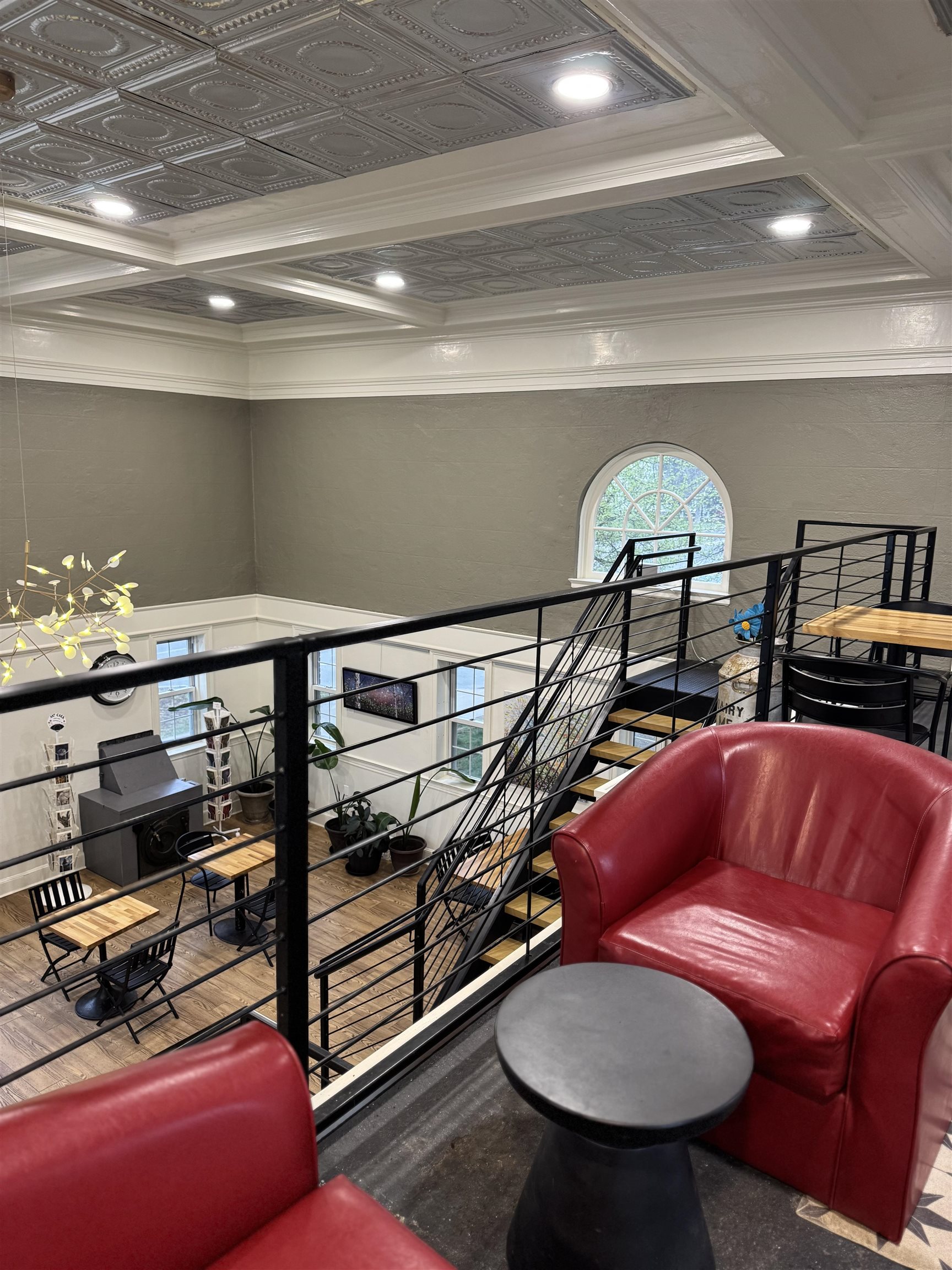 Mezzanine lounge with red leather armchairs, black railings, ornate ceiling, and an arched window.