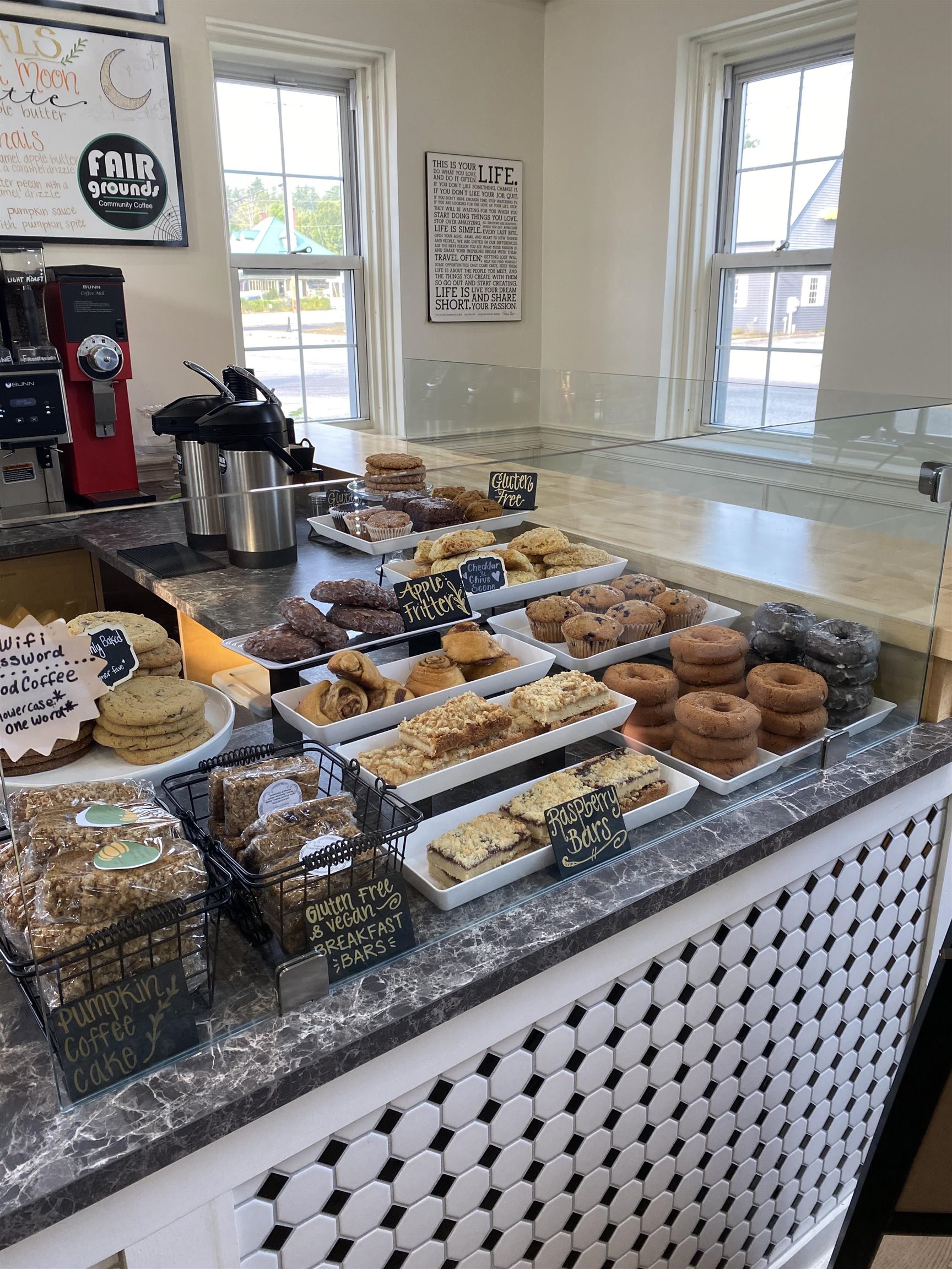 Bakery counter displaying assorted pastries and coffee equipment, with a black-and-white tiled front.