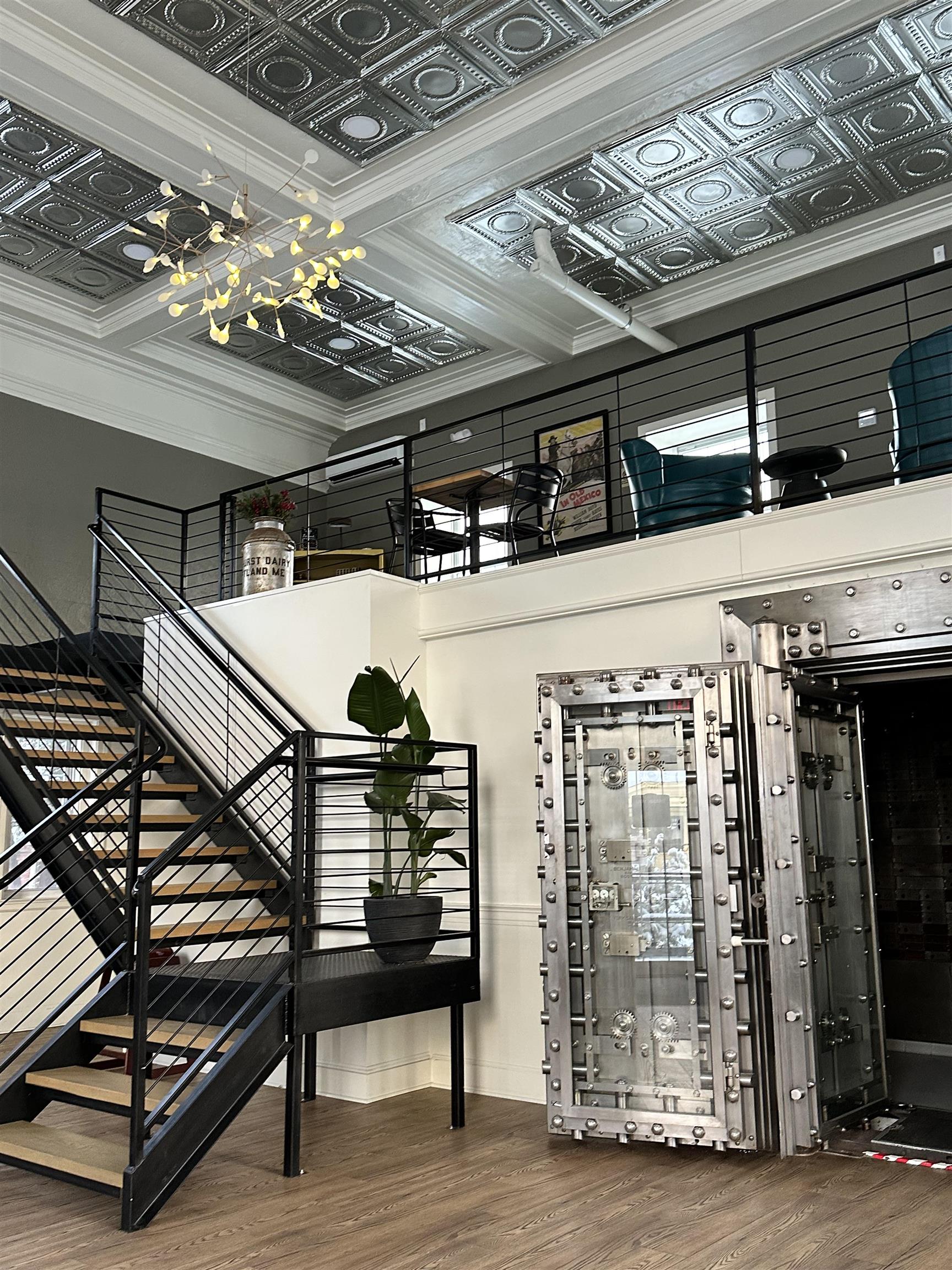 Commercial interior with a massive metal vault door, black staircase, and ornate pressed-tin ceiling.