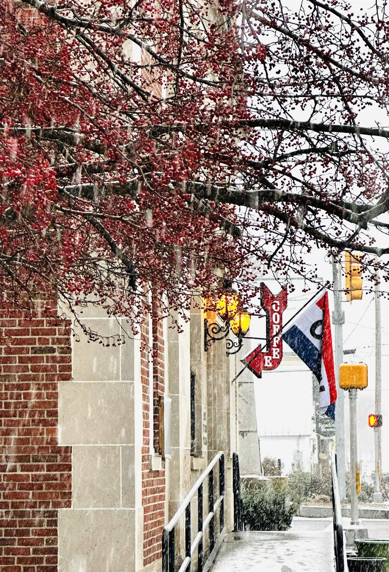 Brick and stone storefront in falling snow, framed by red berries and a vertical COFFEE sign.