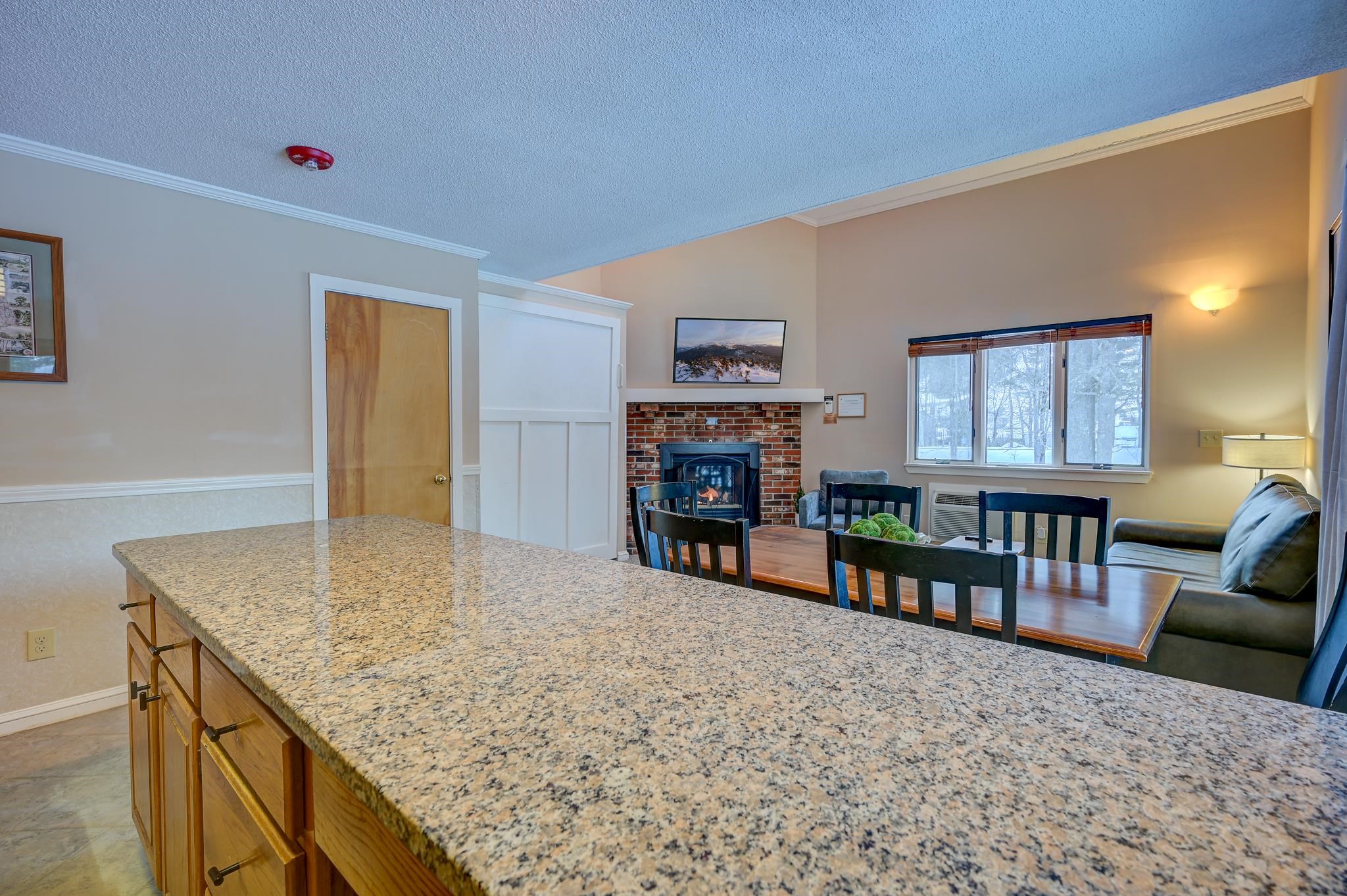 Granite kitchen island overlooking a dining area and living room with a brick fireplace and snowy views.