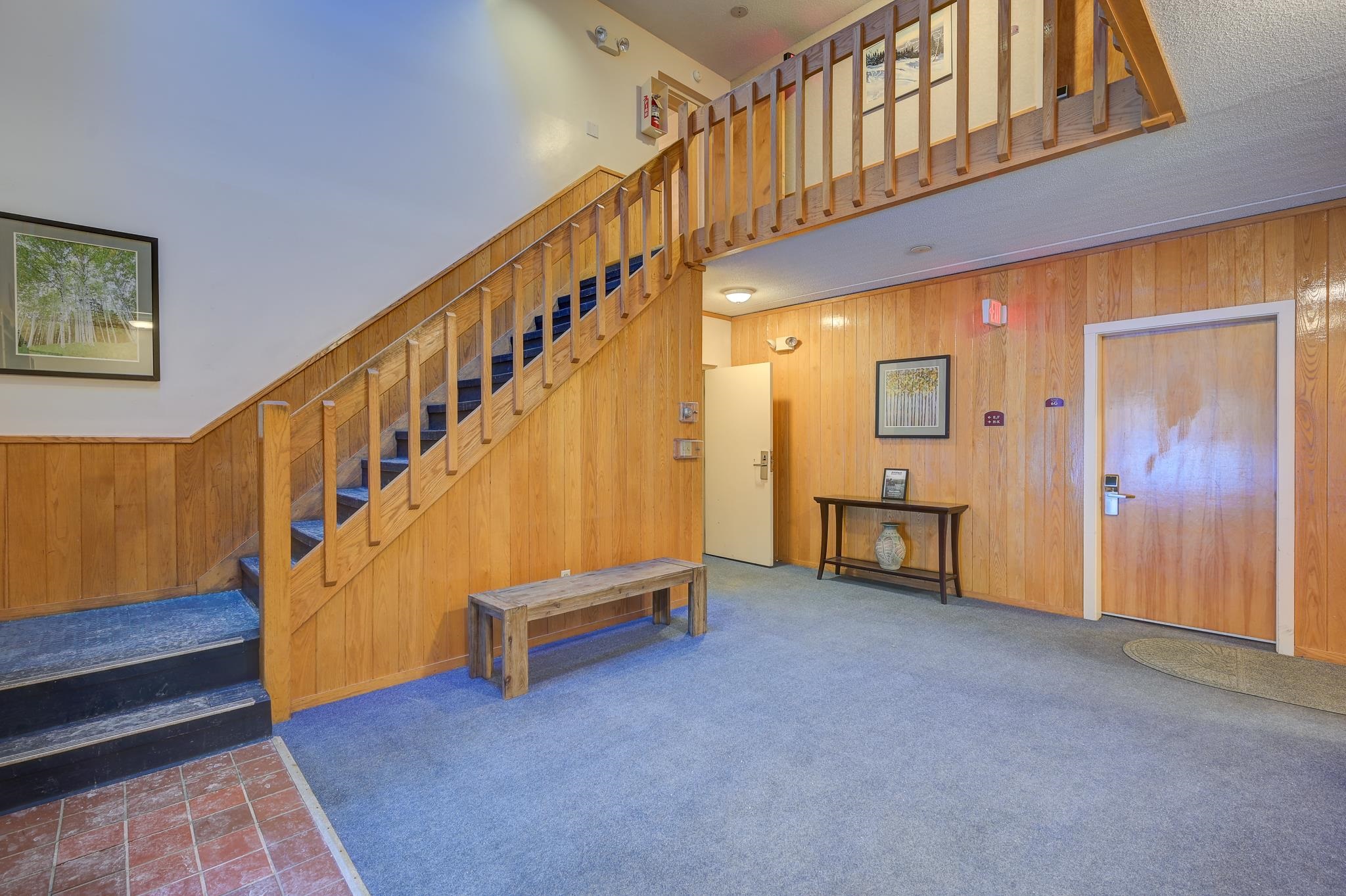 Wood-paneled entry hall with carpeted stairs, an upper landing, and a wooden bench.