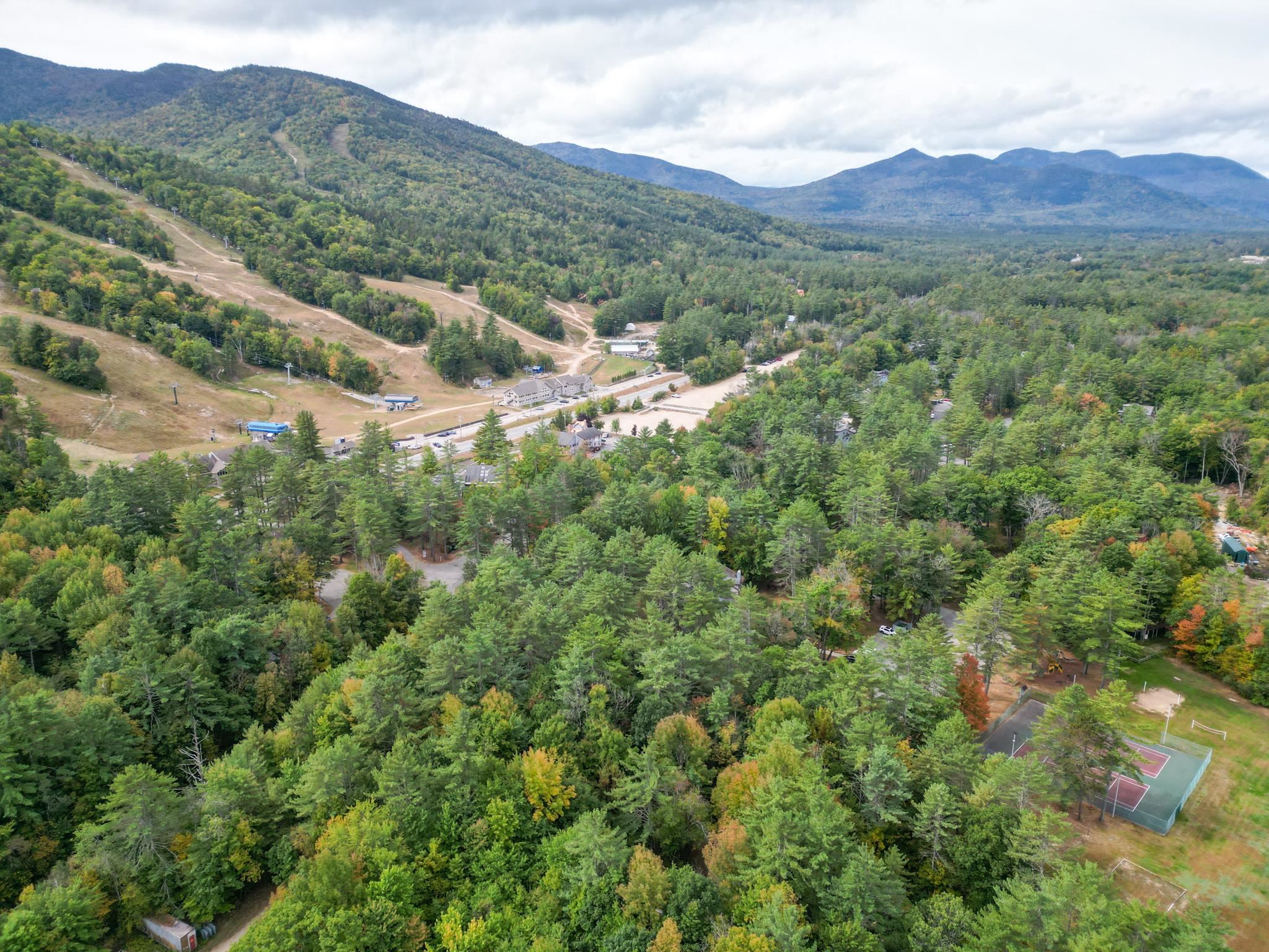 Aerial view of a wooded mountain resort with ski trails, tennis courts and mountain ranges.