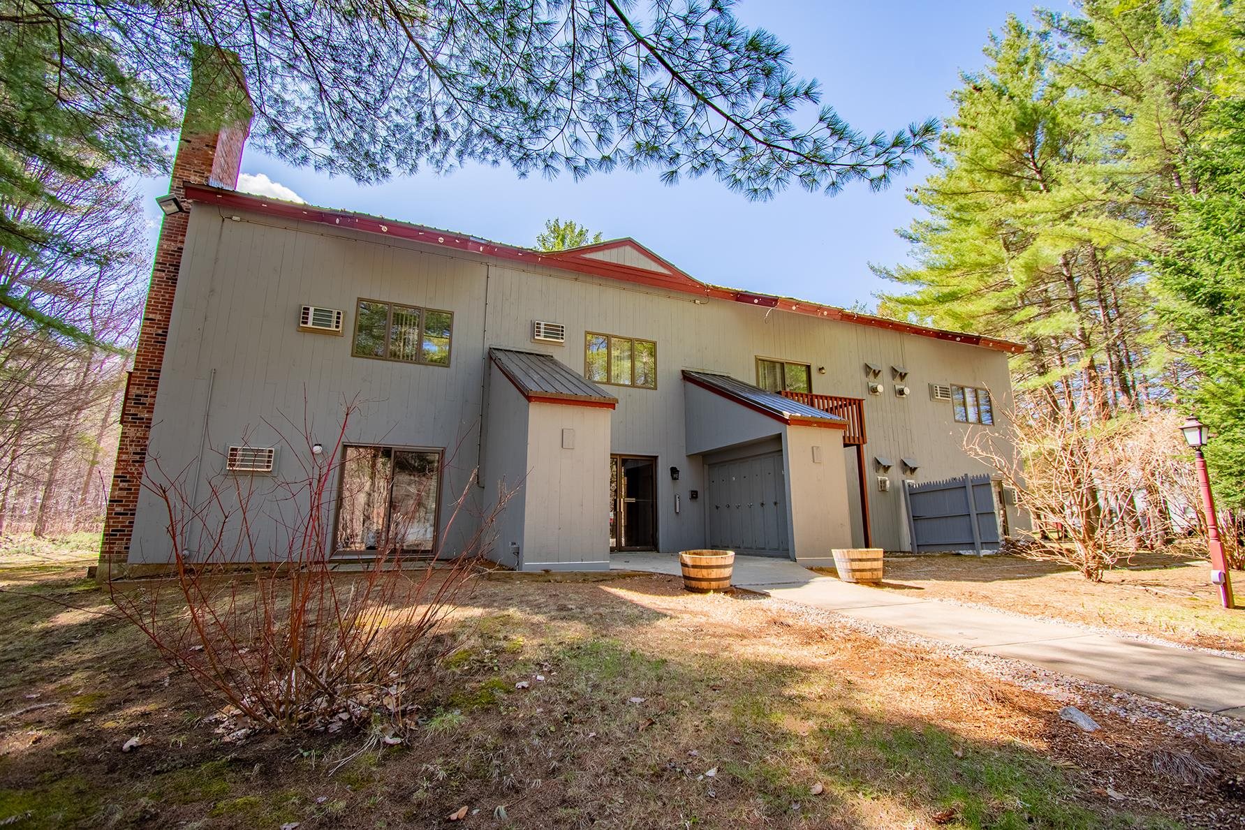 Gray multi-unit building with red roof trim and brick chimney, surrounded by pine trees.