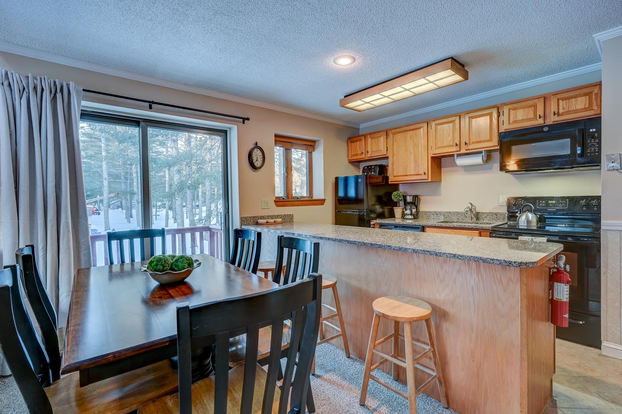 Kitchen and dining area with a granite breakfast bar, wood cabinets, and snowy trees outside the sliding door.