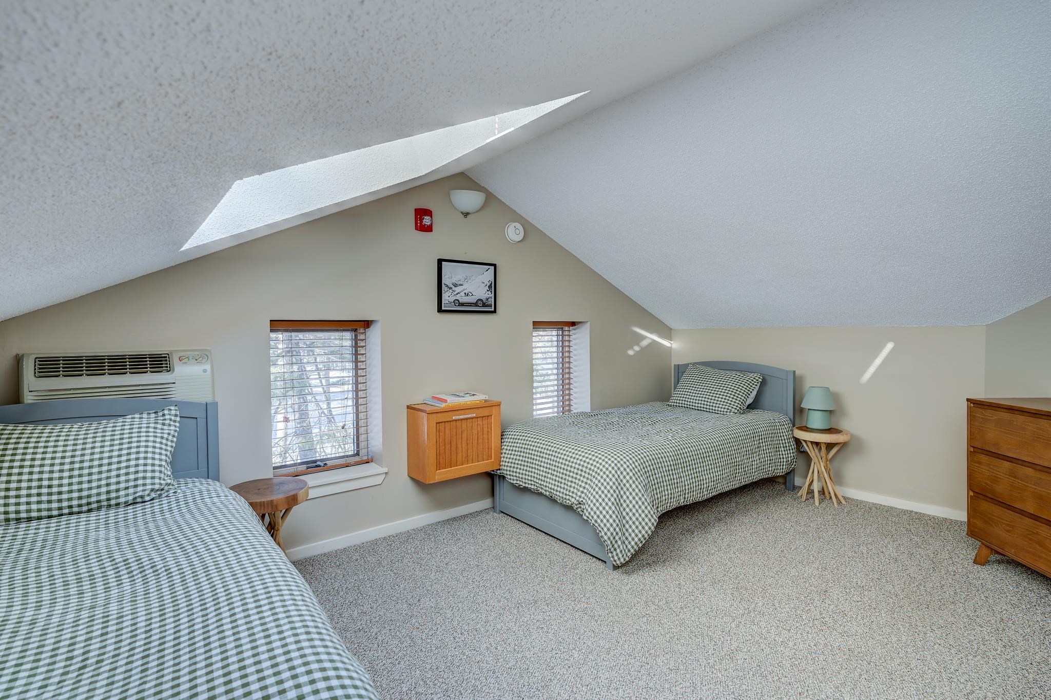 Furnished attic bedroom with two green-and-white gingham beds and narrow windows.