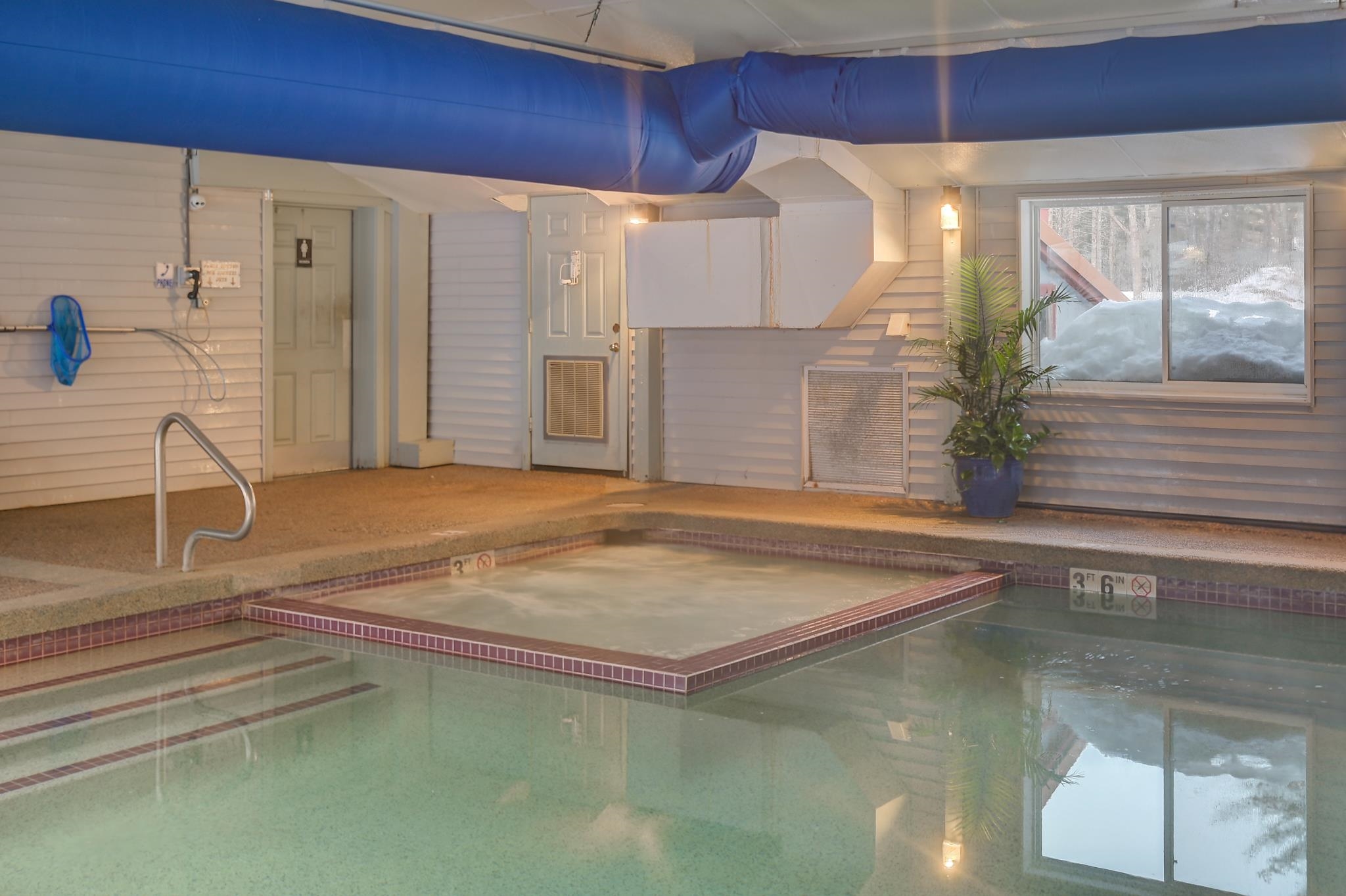 Indoor pool with a raised shallow wading area, tiled steps, and a large blue overhead duct.