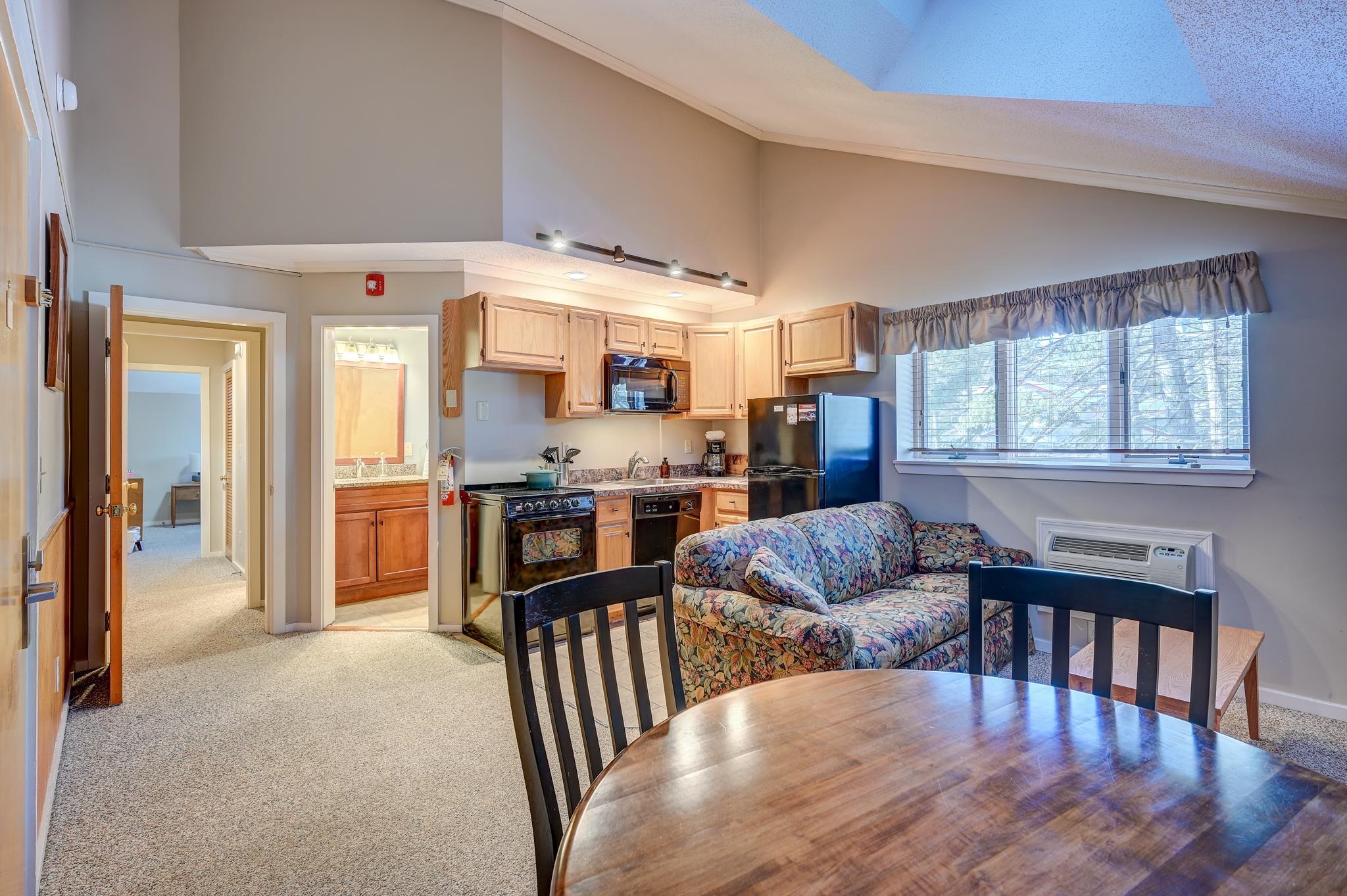 Open-plan living area with a vaulted ceiling, skylight, floral sofa, and adjoining kitchen.