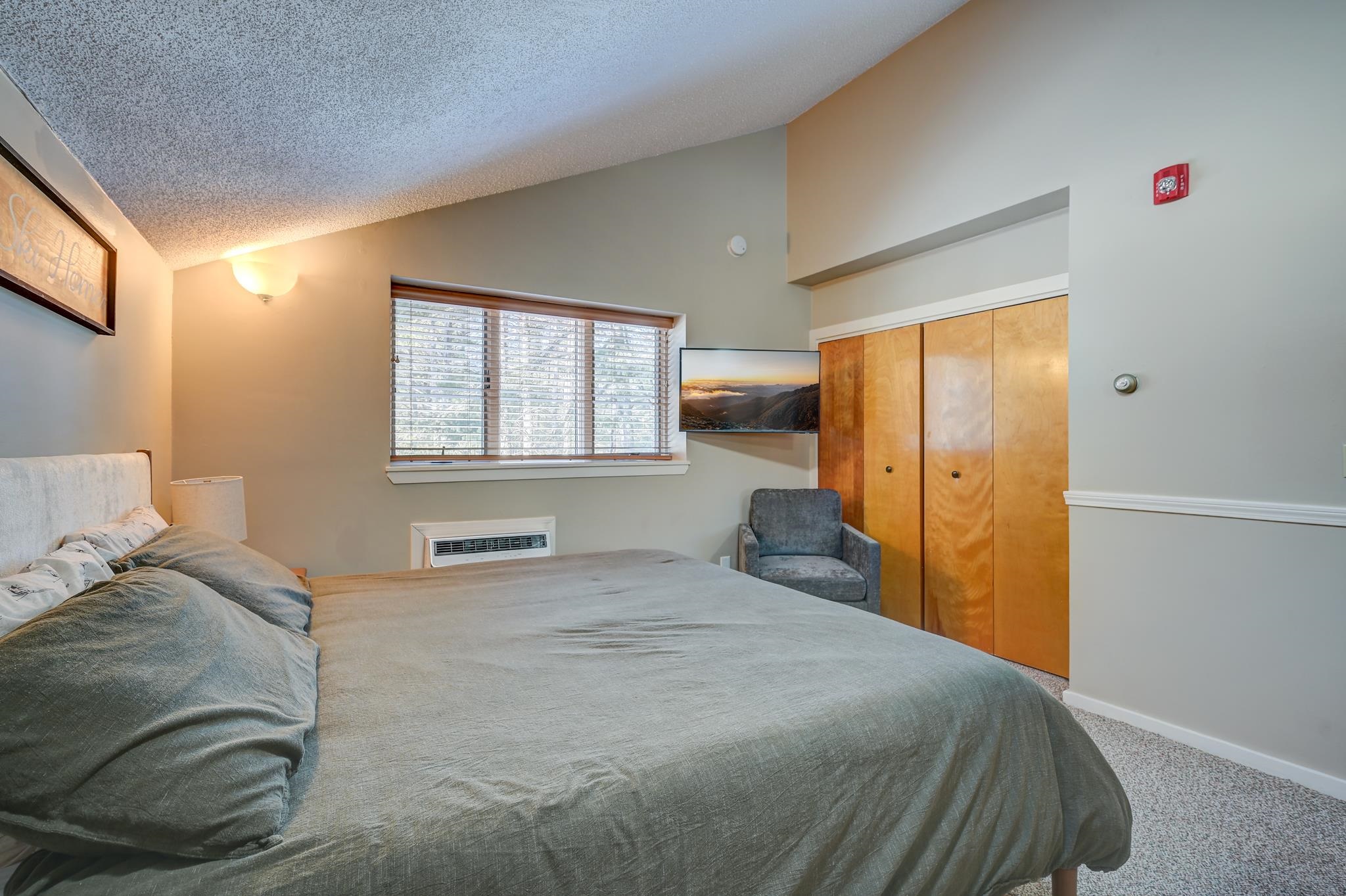 Bedroom with a large gray-covered bed, wood closet doors, and a wall-mounted television.