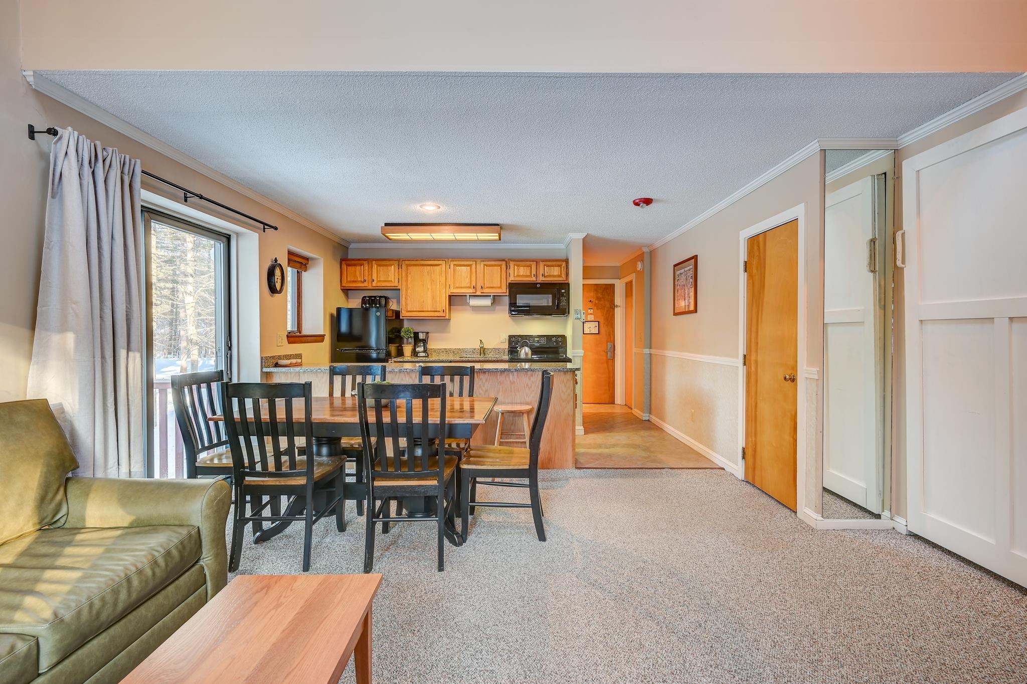 Open-plan condo kitchen and dining area with wood cabinets, a breakfast bar, and a snowy view through the sliding door.
