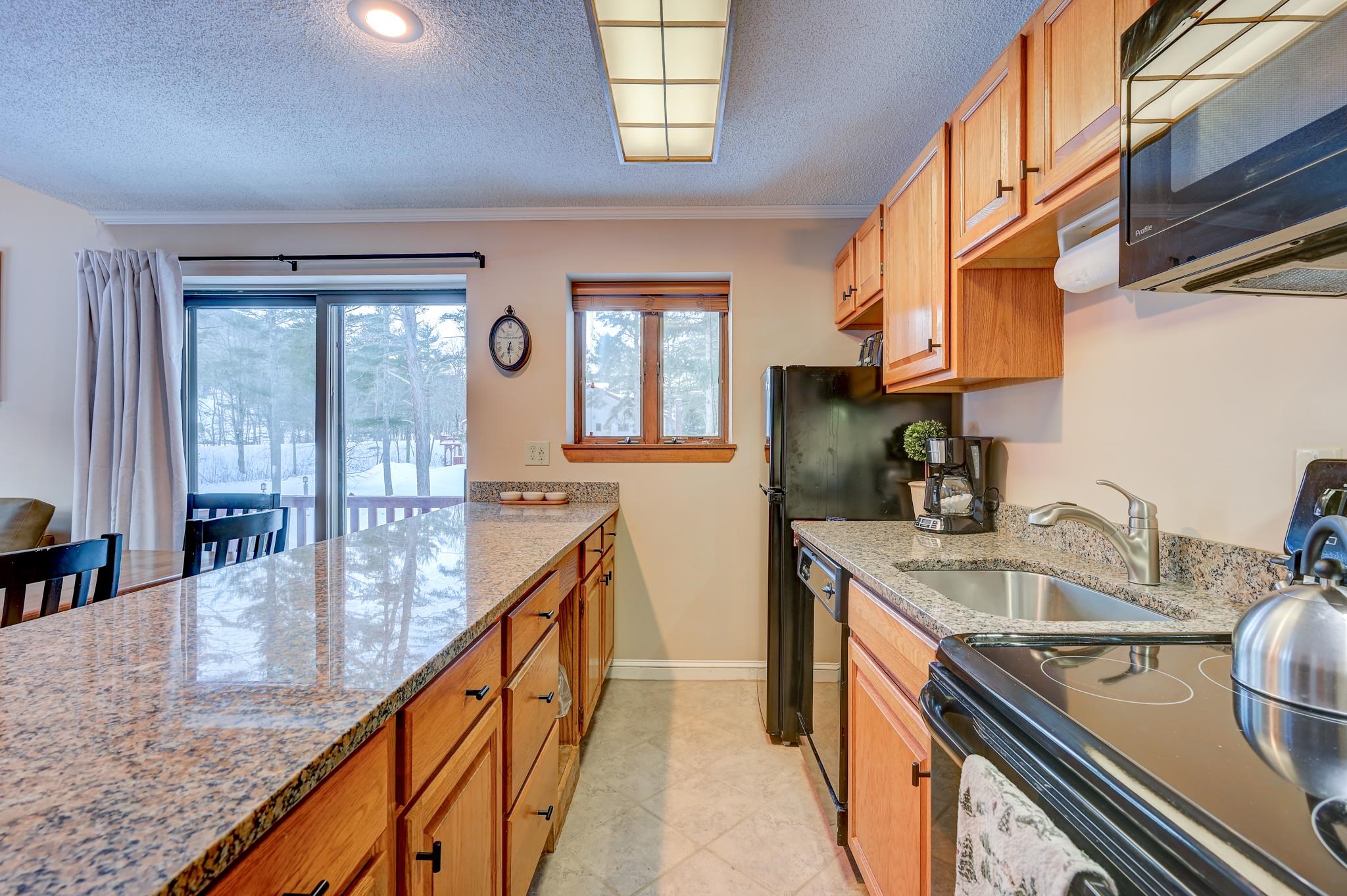 Condominium kitchen with granite counters, wood cabinets, and sliding doors overlooking snowy woods.