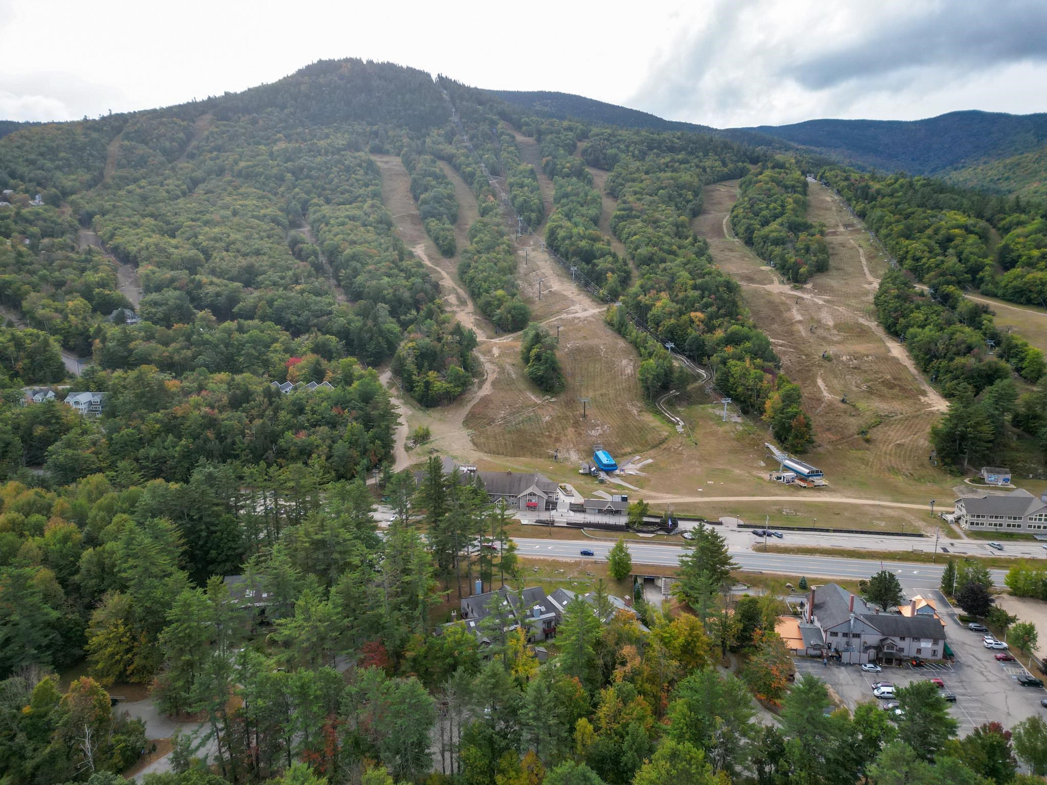 Aerial view of ski trails crossing a forested mountain above resort buildings.