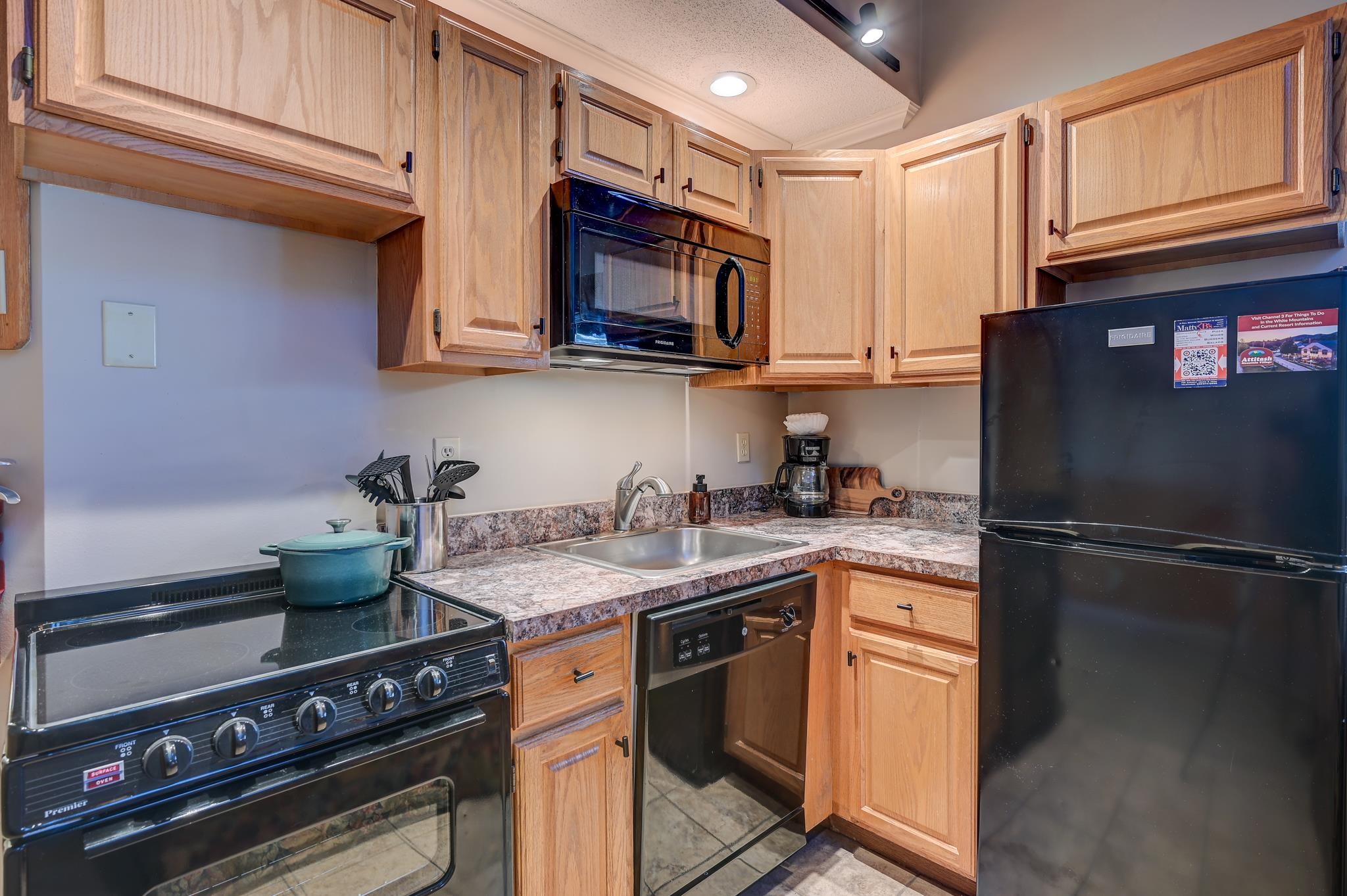 Kitchen with honey-toned cabinets, mottled countertops, and black appliances.