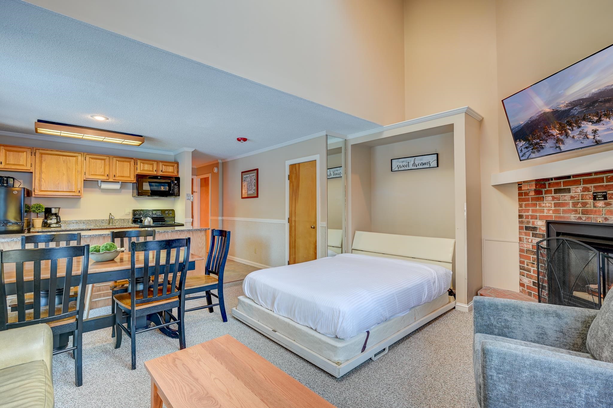 Furnished studio with a bed beside the kitchen and dining area, plus a brick fireplace.