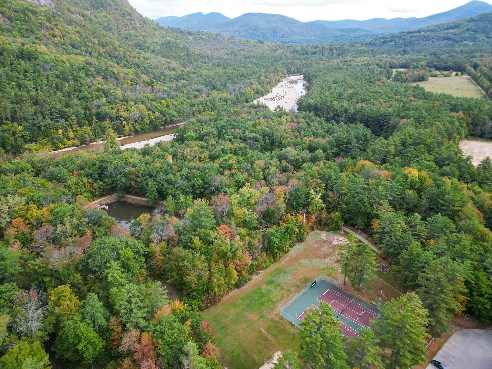 Aerial view of wooded mountain community with a winding river and tennis courts