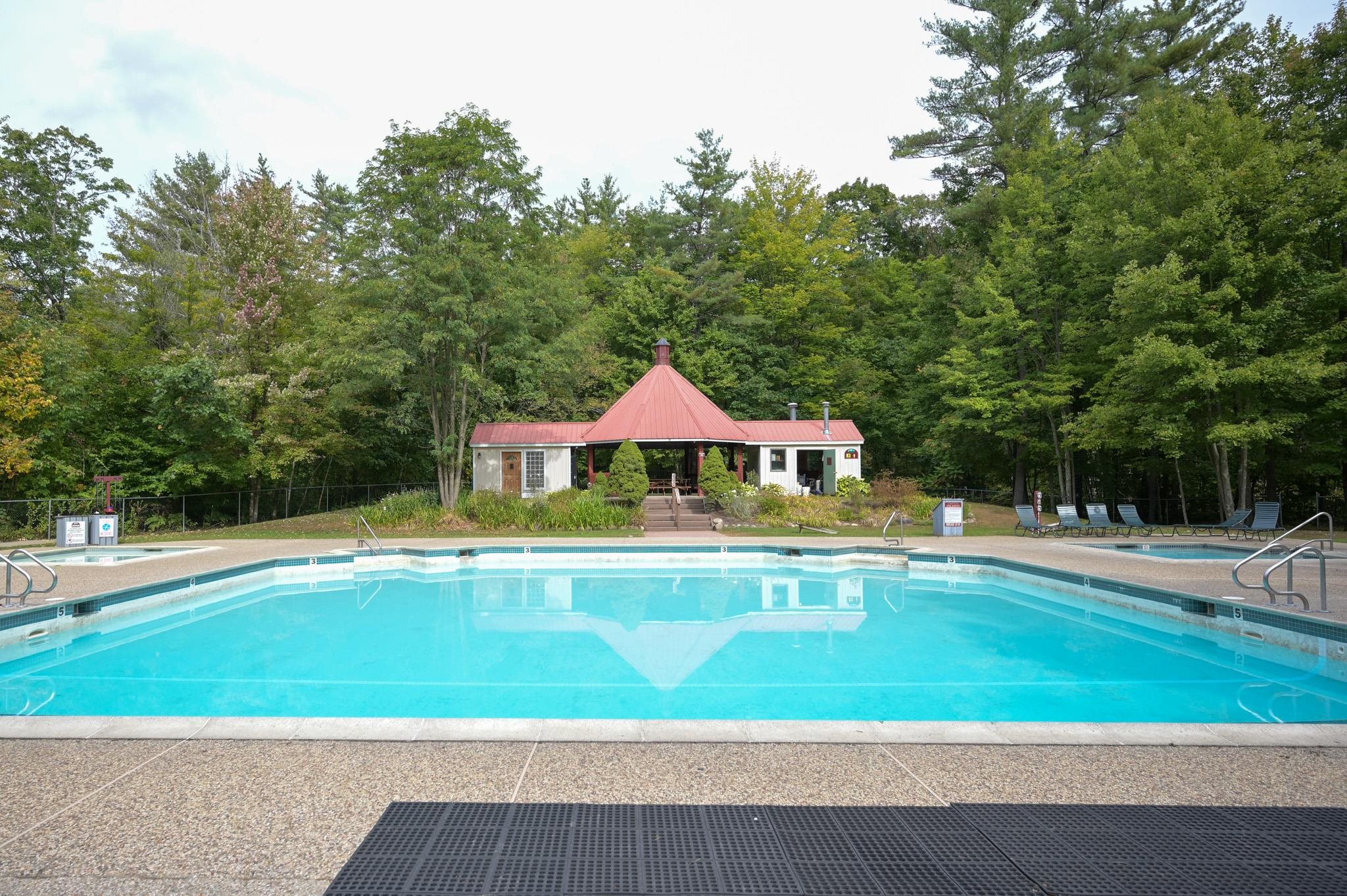 Outdoor pool with a red-roofed pool house and trees behind it.
