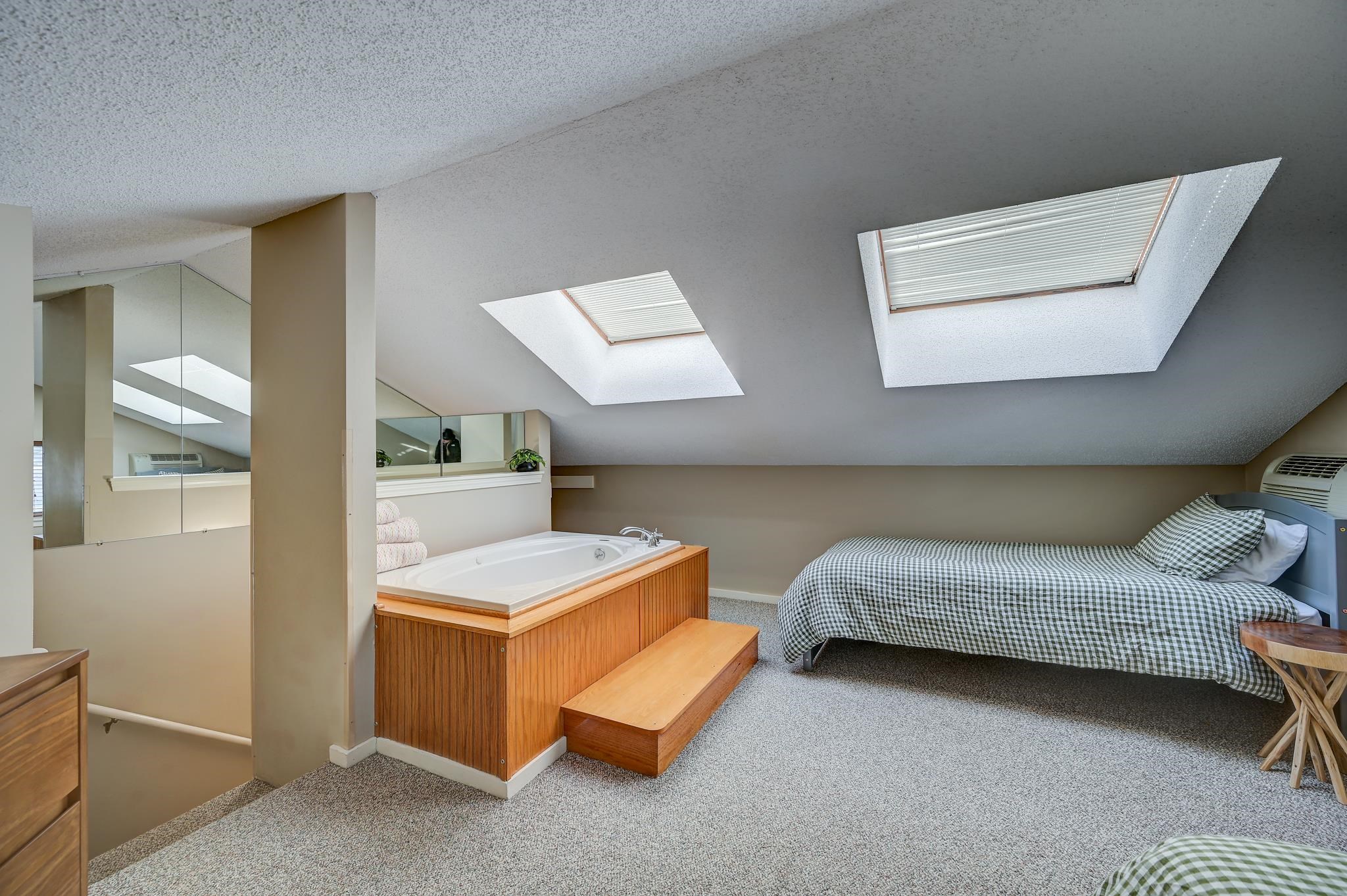 Attic bedroom with skylights, a twin bed, and a built-in soaking tub.