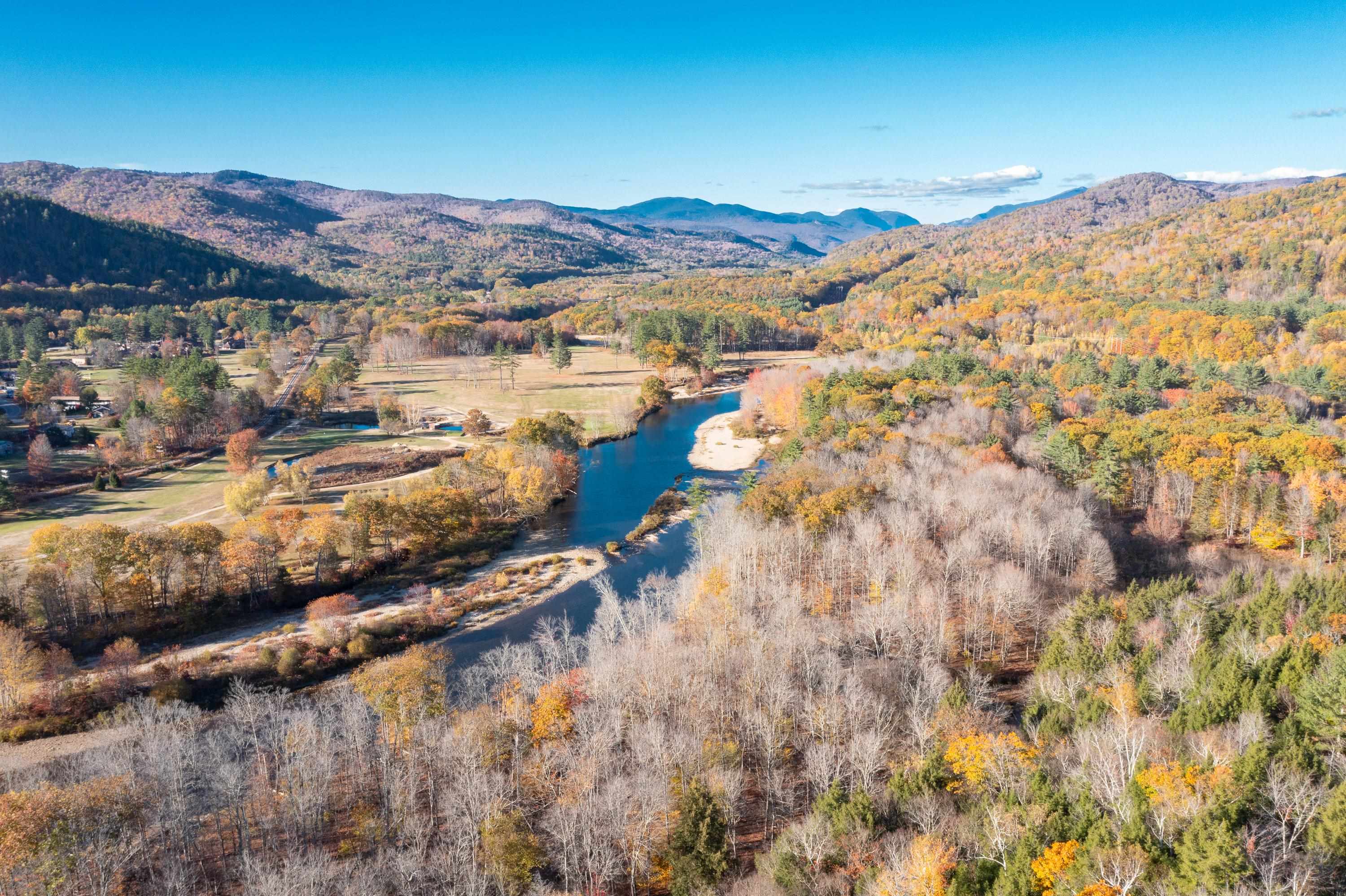 Aerial view of a river winding through an autumn valley, with open fields and mountain ridges.