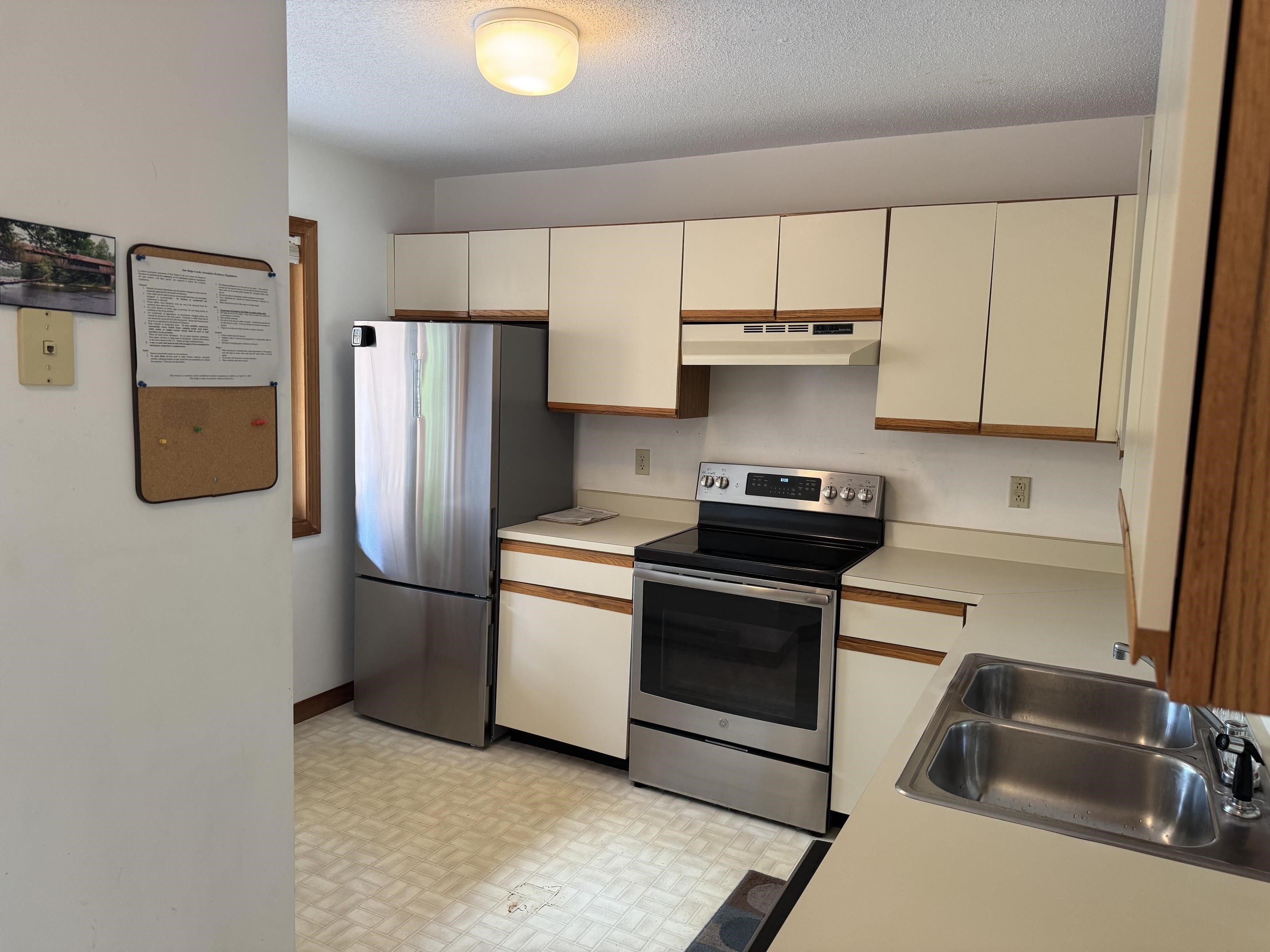 Compact kitchen with cream cabinets, stainless-steel appliances, and a double-basin sink.