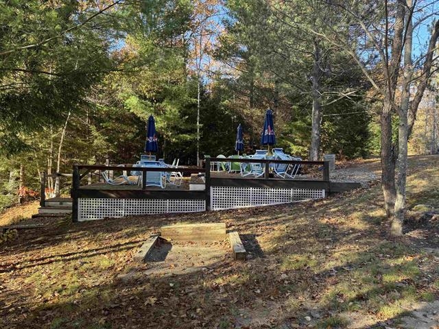 Raised deck with blue umbrellas and lounge chairs among autumn trees.