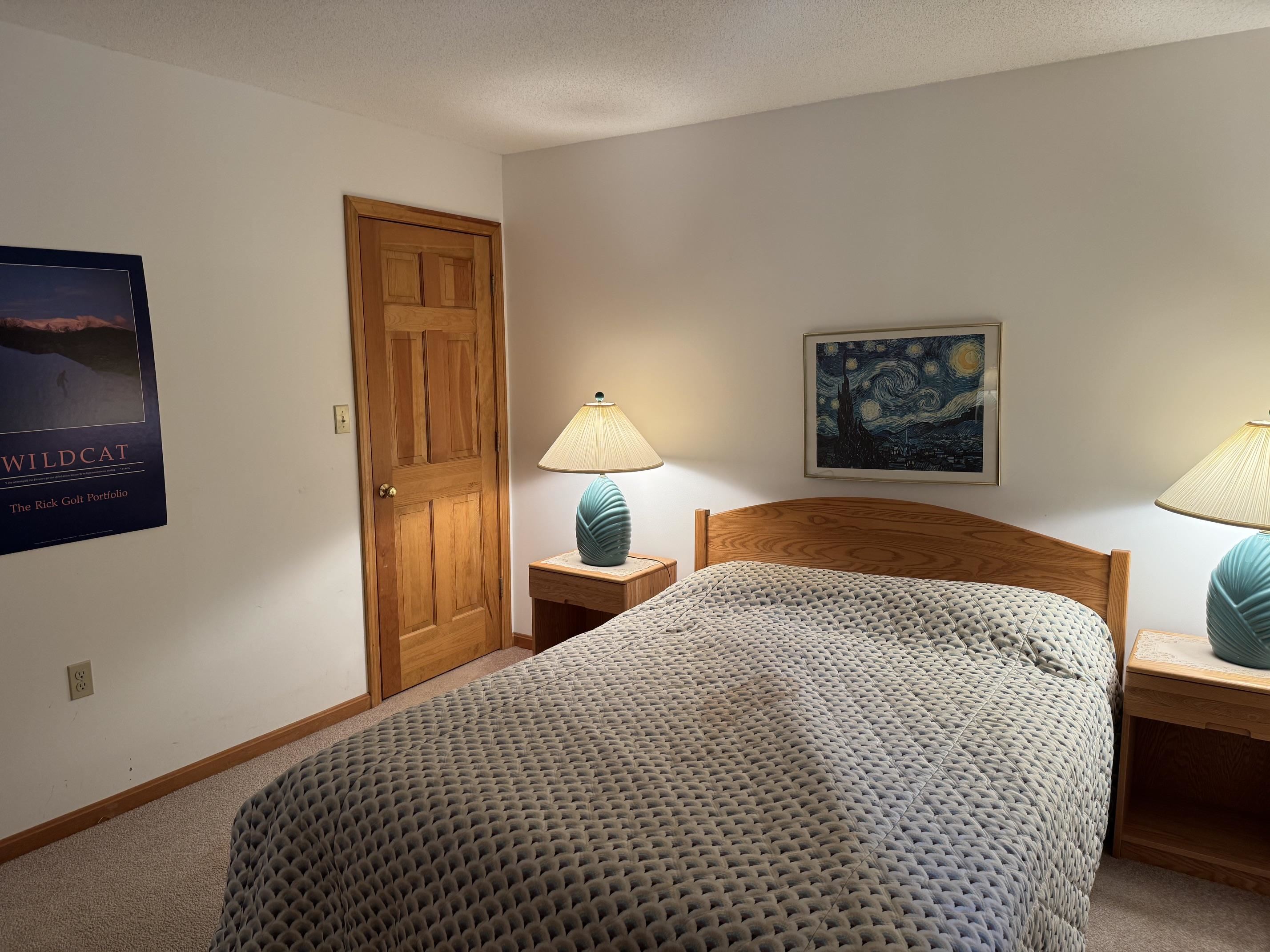 Bedroom with a gray patterned bedspread, wooden headboard, and matching nightstands with turquoise lamps.