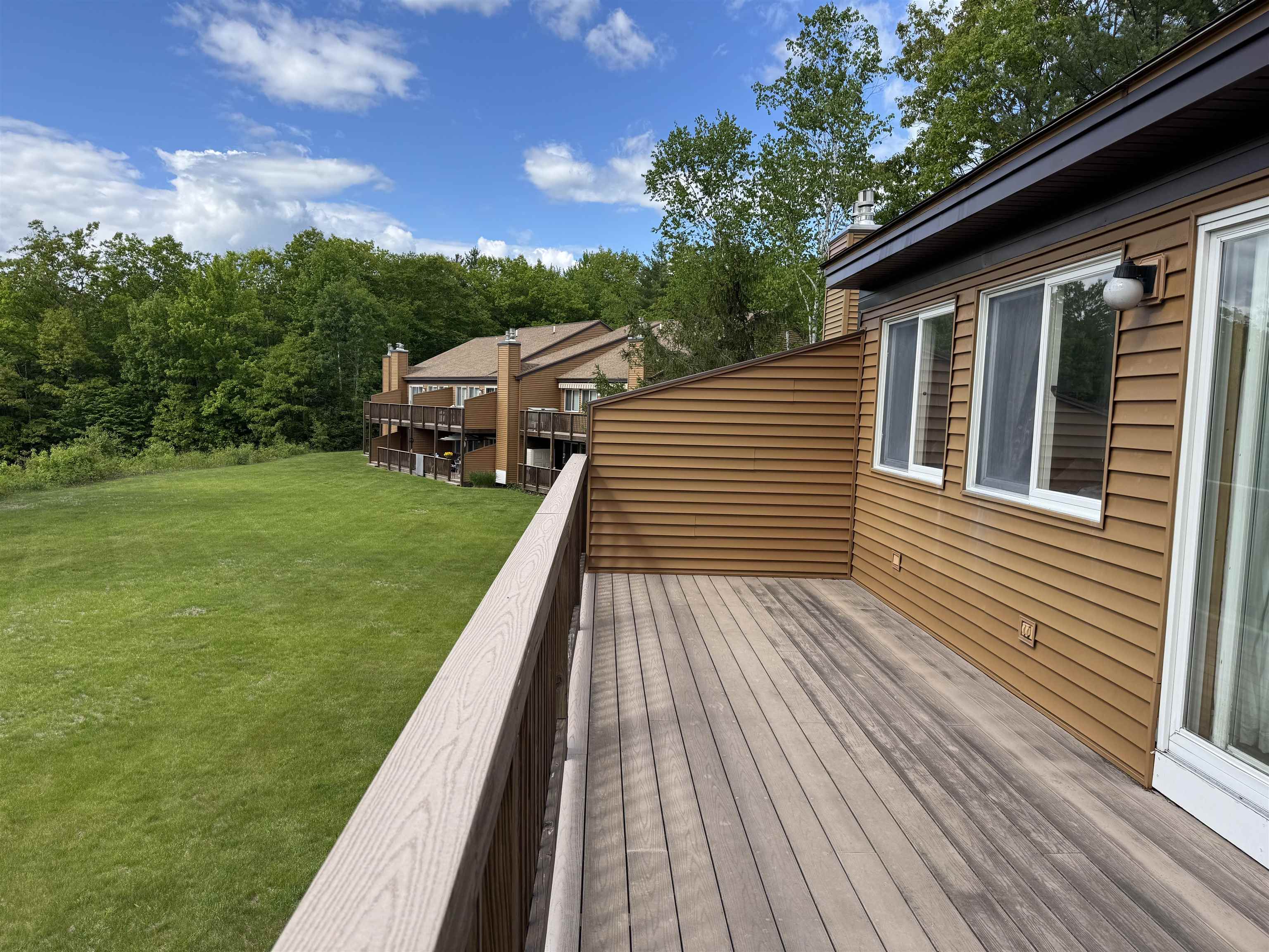 Condominium deck overlooking a green lawn and neighboring units at the tree line.