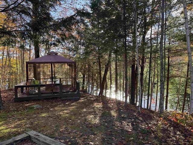 Gazebo on a raised deck among autumn trees, with water visible through the woods.