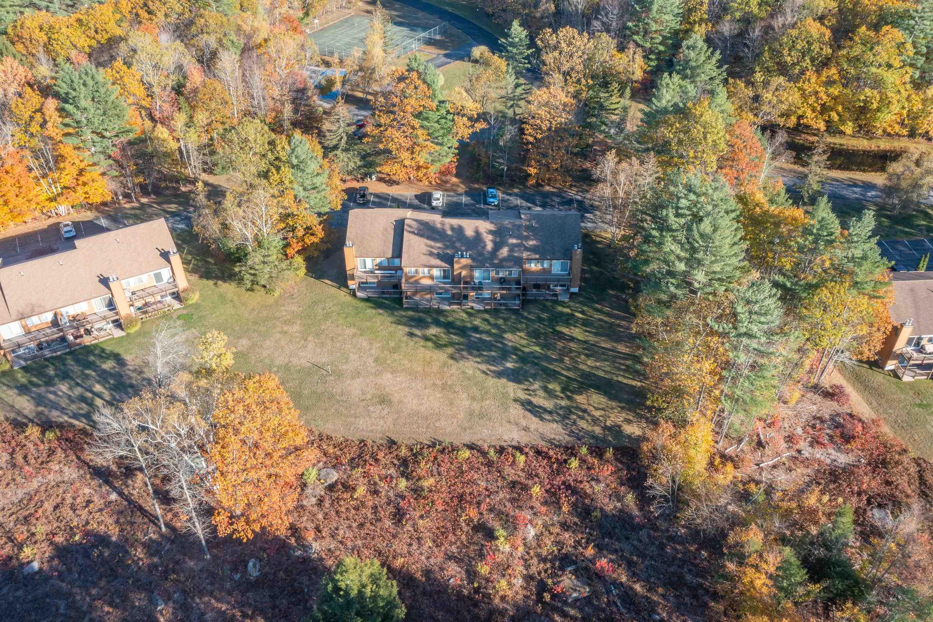 Aerial view of condominium buildings amid colorful autumn trees, with a lawn and tennis courts nearby.