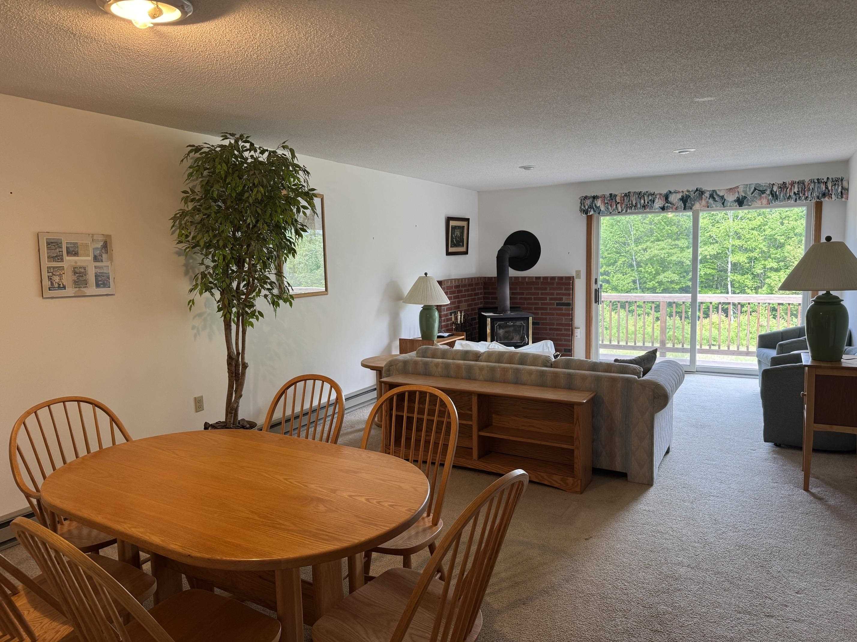 Open-plan dining and living room with a wood stove and sliding doors to a tree-lined deck.