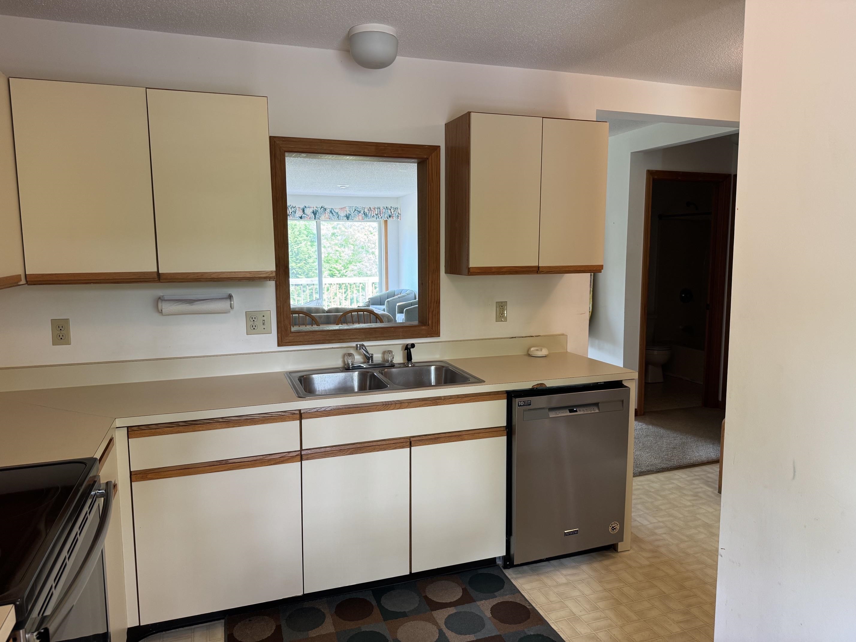 Kitchen with cream and wood-trimmed cabinets, double sink, and dishwasher beside a pass-through mirror.