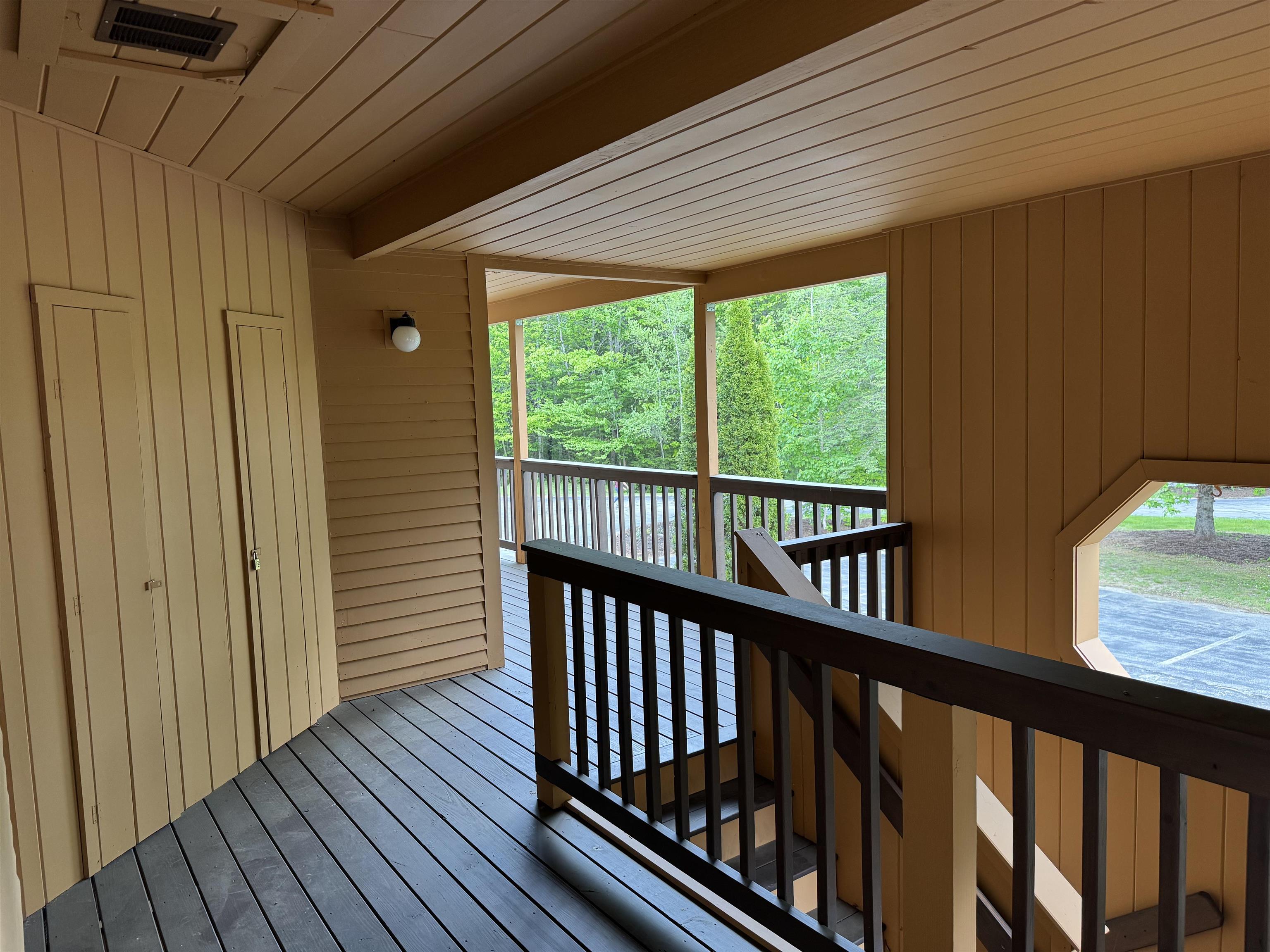 Covered wooden porch with dark railings, stairs, and a leafy tree view.
