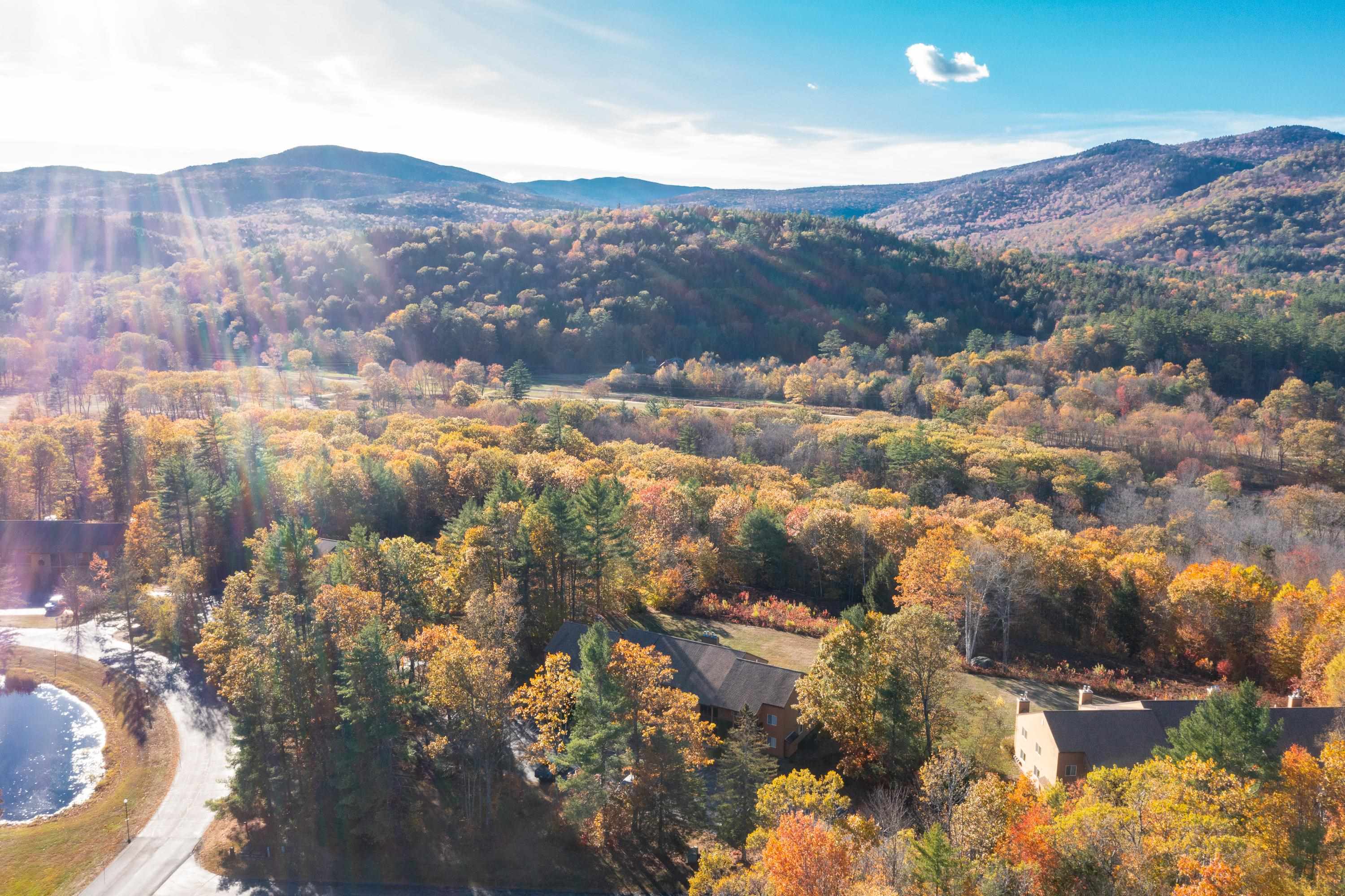 Aerial view of homes and a pool amid autumn foliage, with mountain ridges beyond.