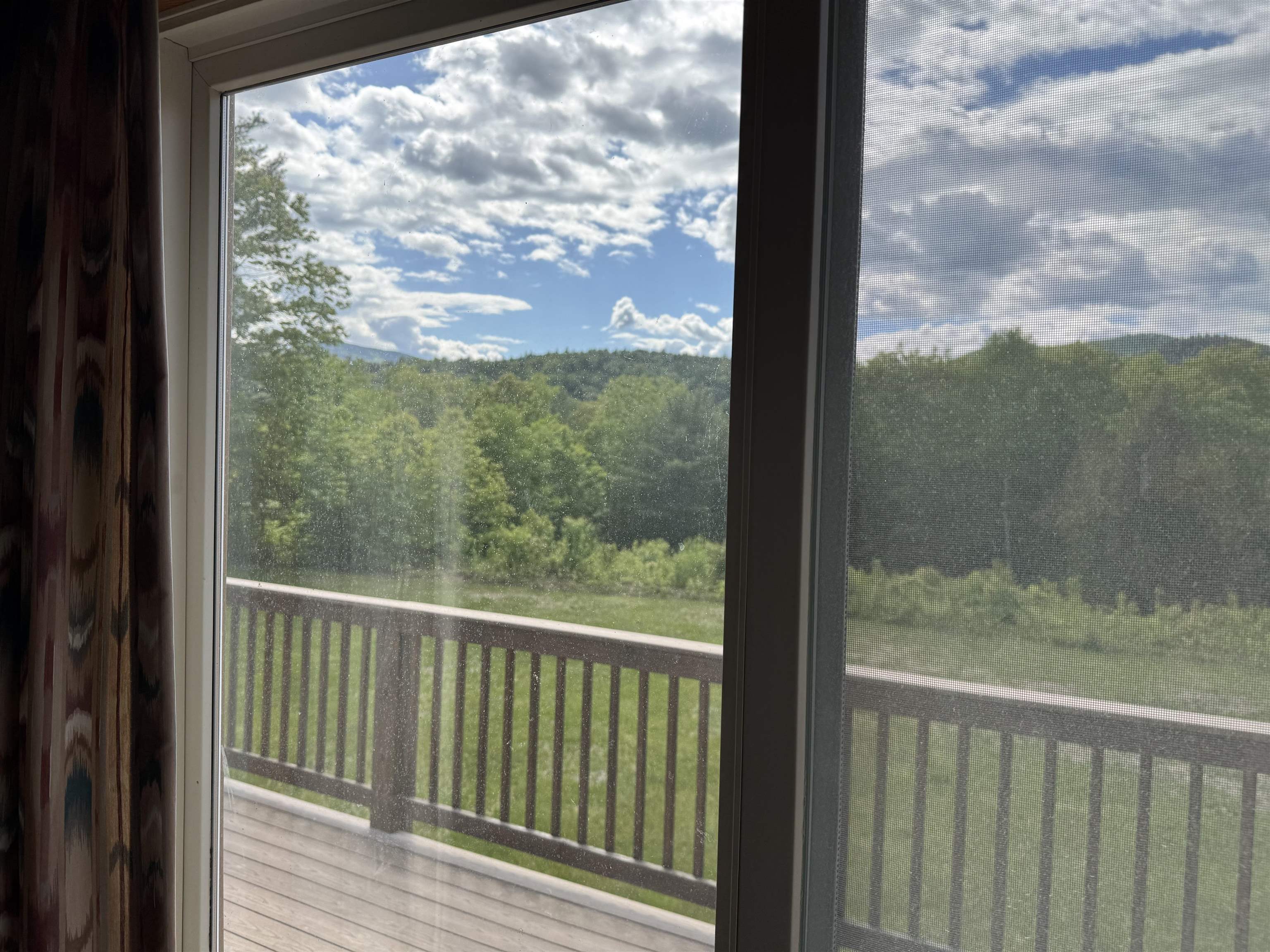 Wooden balcony overlooking a lawn and wooded hills, seen through a sliding glass door.