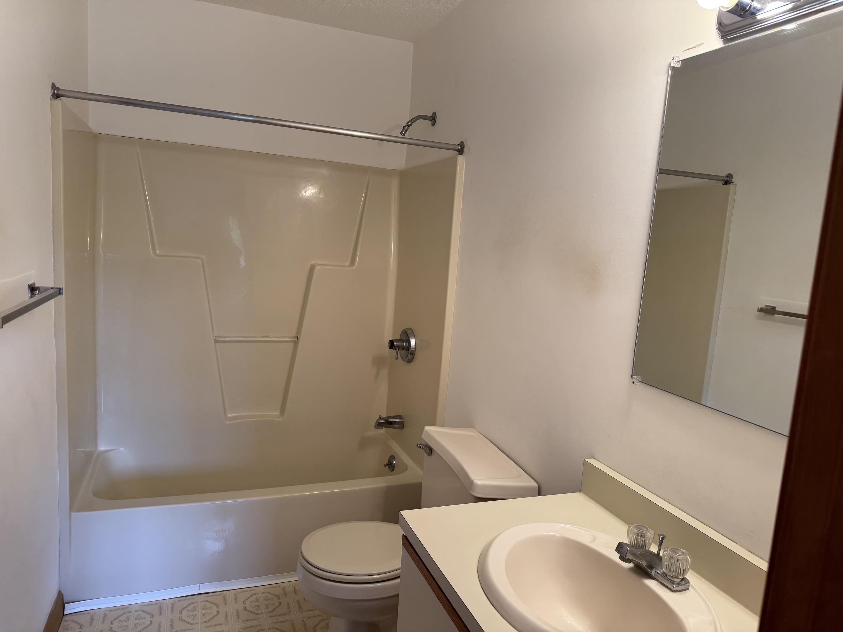 Bathroom with a beige tub and shower, toilet, and vanity with an oval sink.