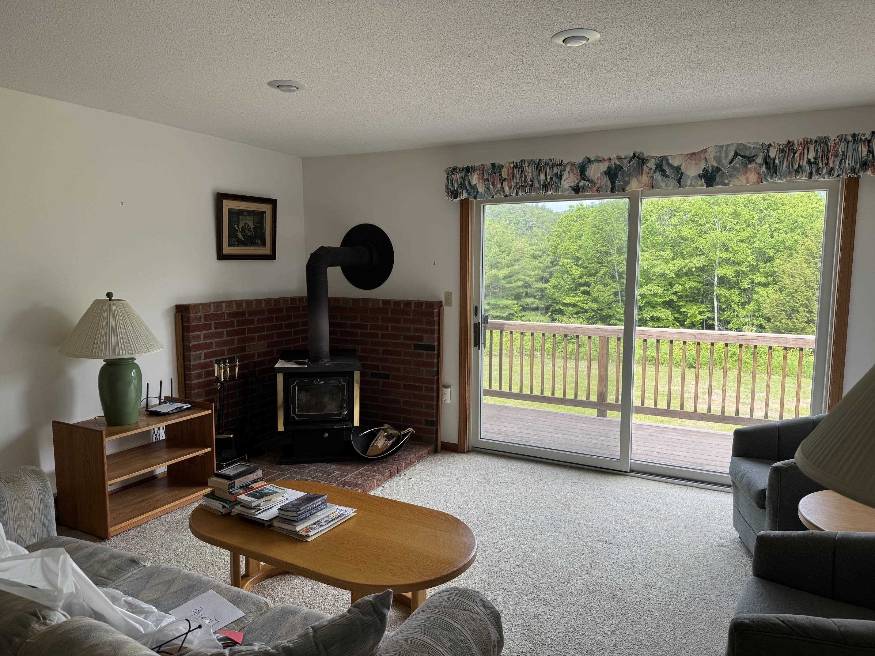 Living room with a brick hearth and wood stove beside sliding doors to a wooded deck.