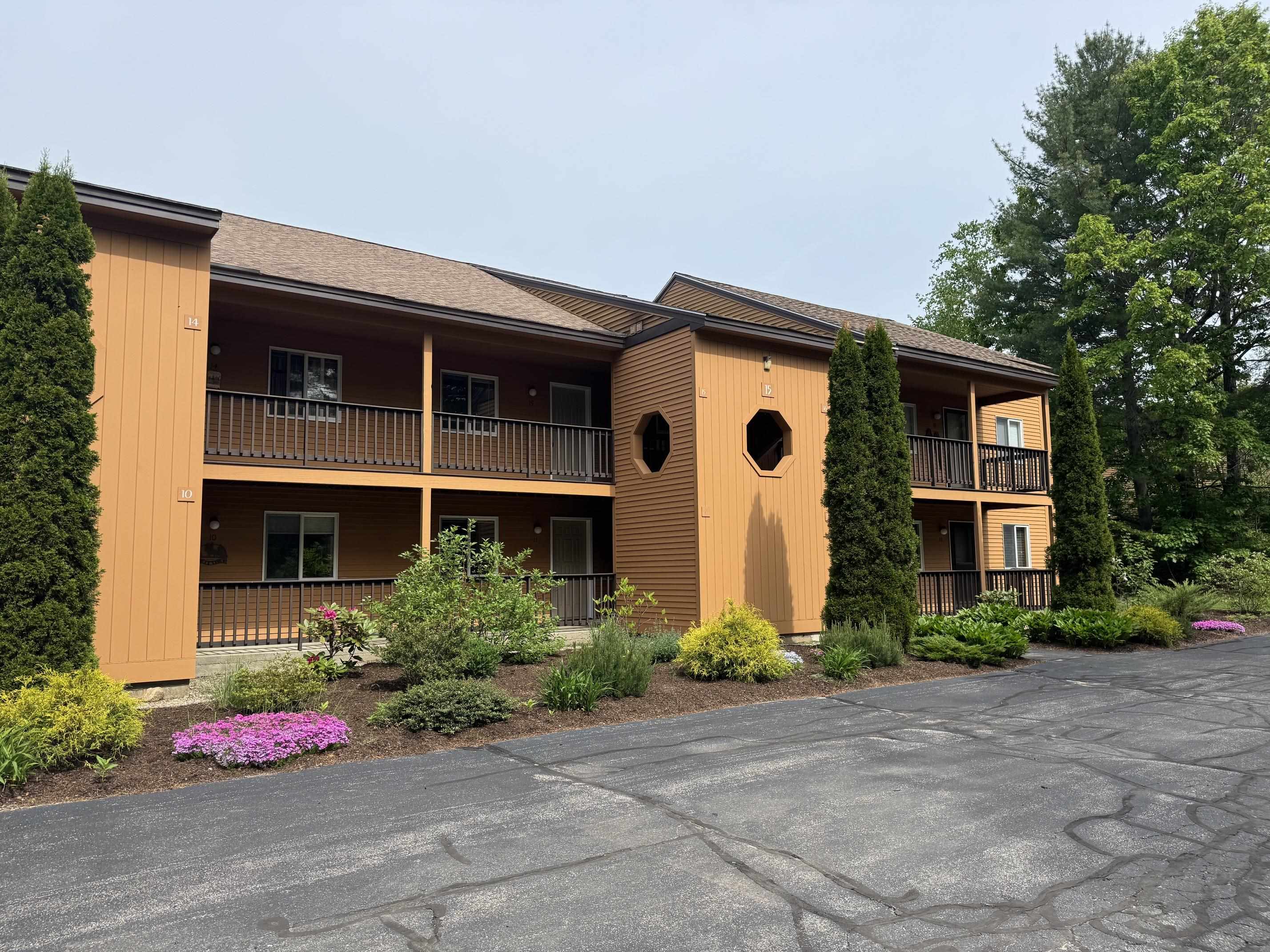 Two-story condominium building with covered balconies, octagonal windows, and landscaped flower beds.