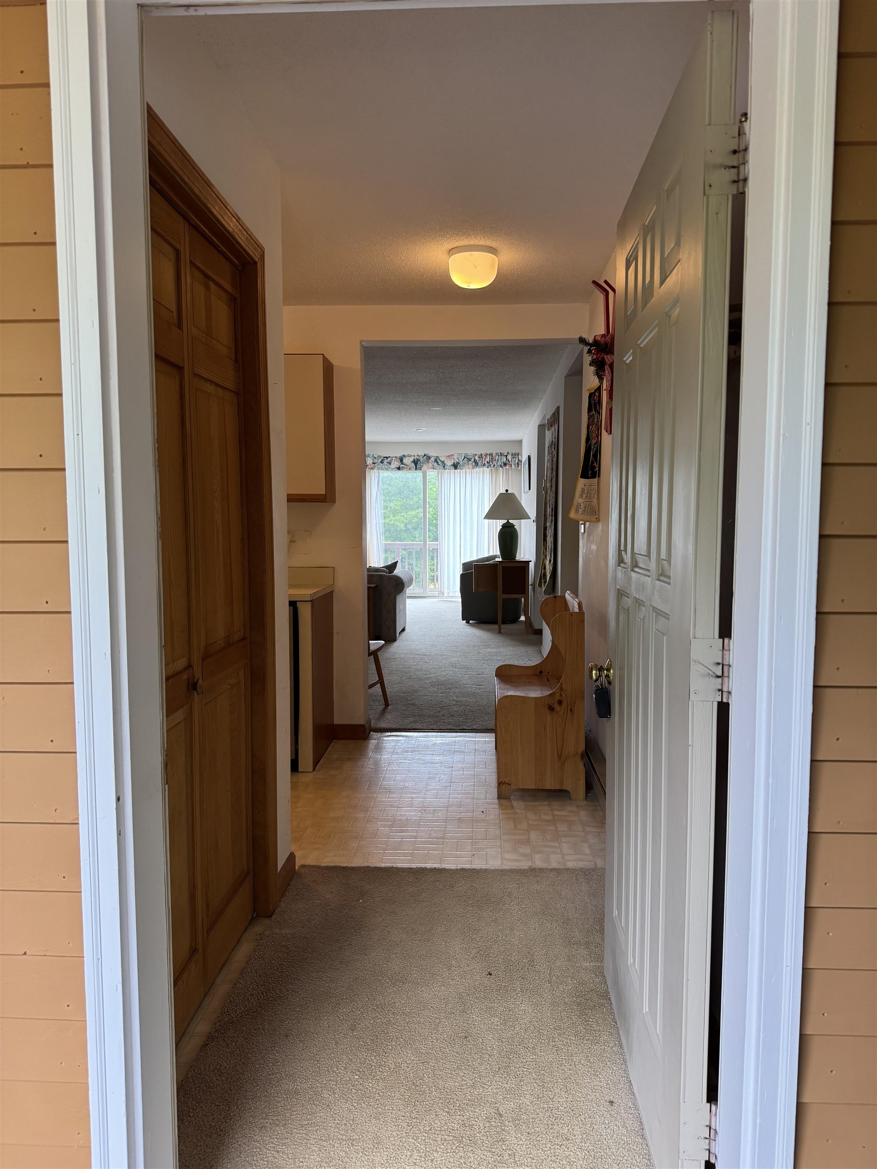 Entry hallway with wood cabinetry leads to a furnished living area and bright sliding glass doors.