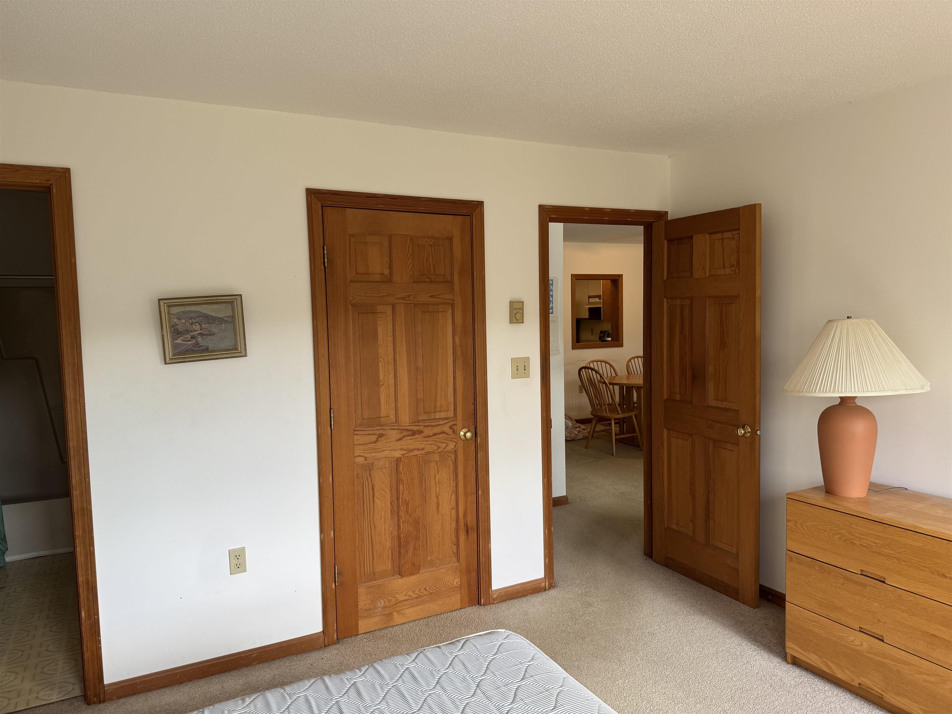 Bedroom with wood-paneled doors, a dresser and lamp, and an open doorway to the dining area.