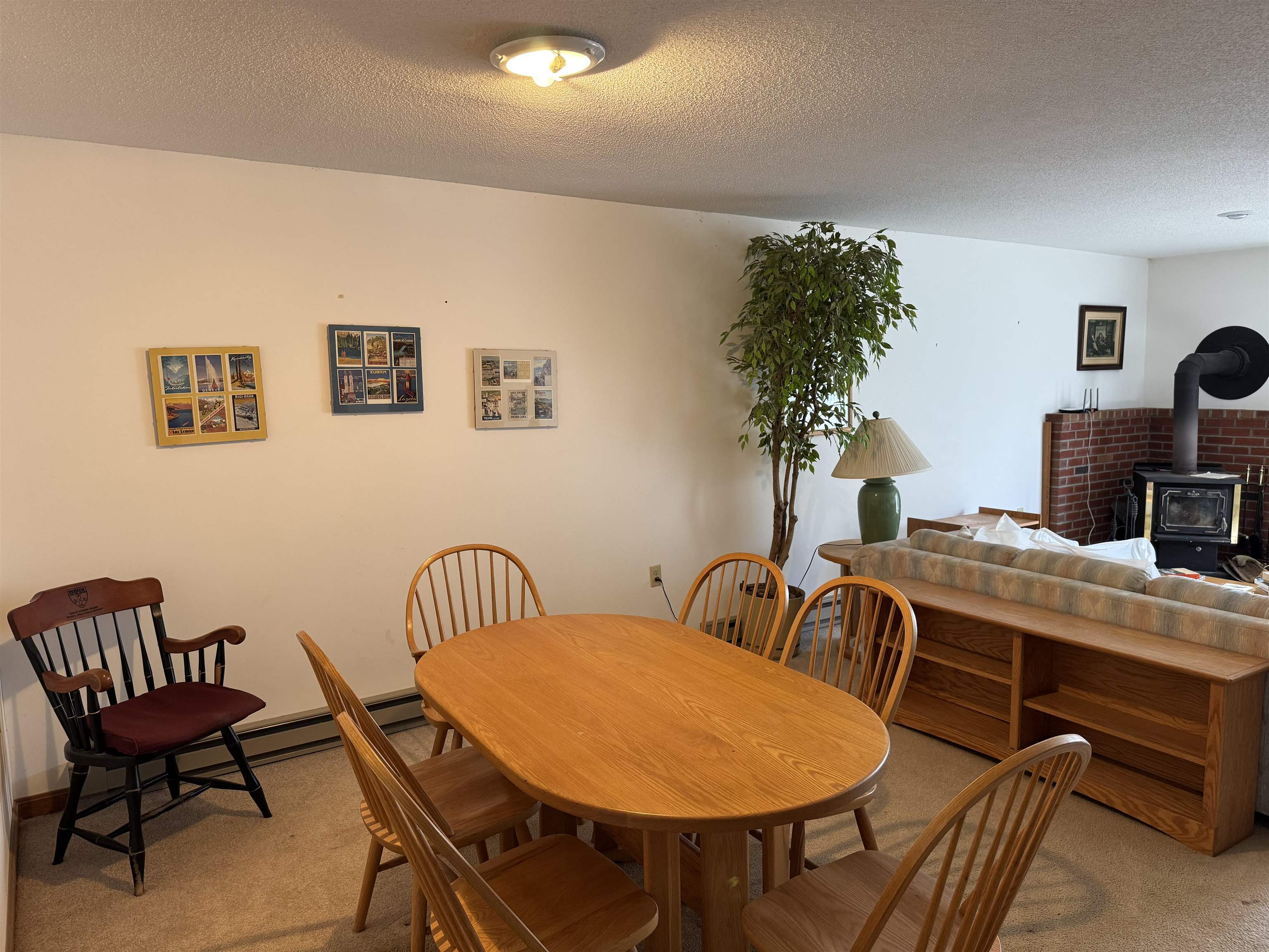 Dining area with an oval wooden table, spindle-back chairs, and a wood-burning stove nearby.