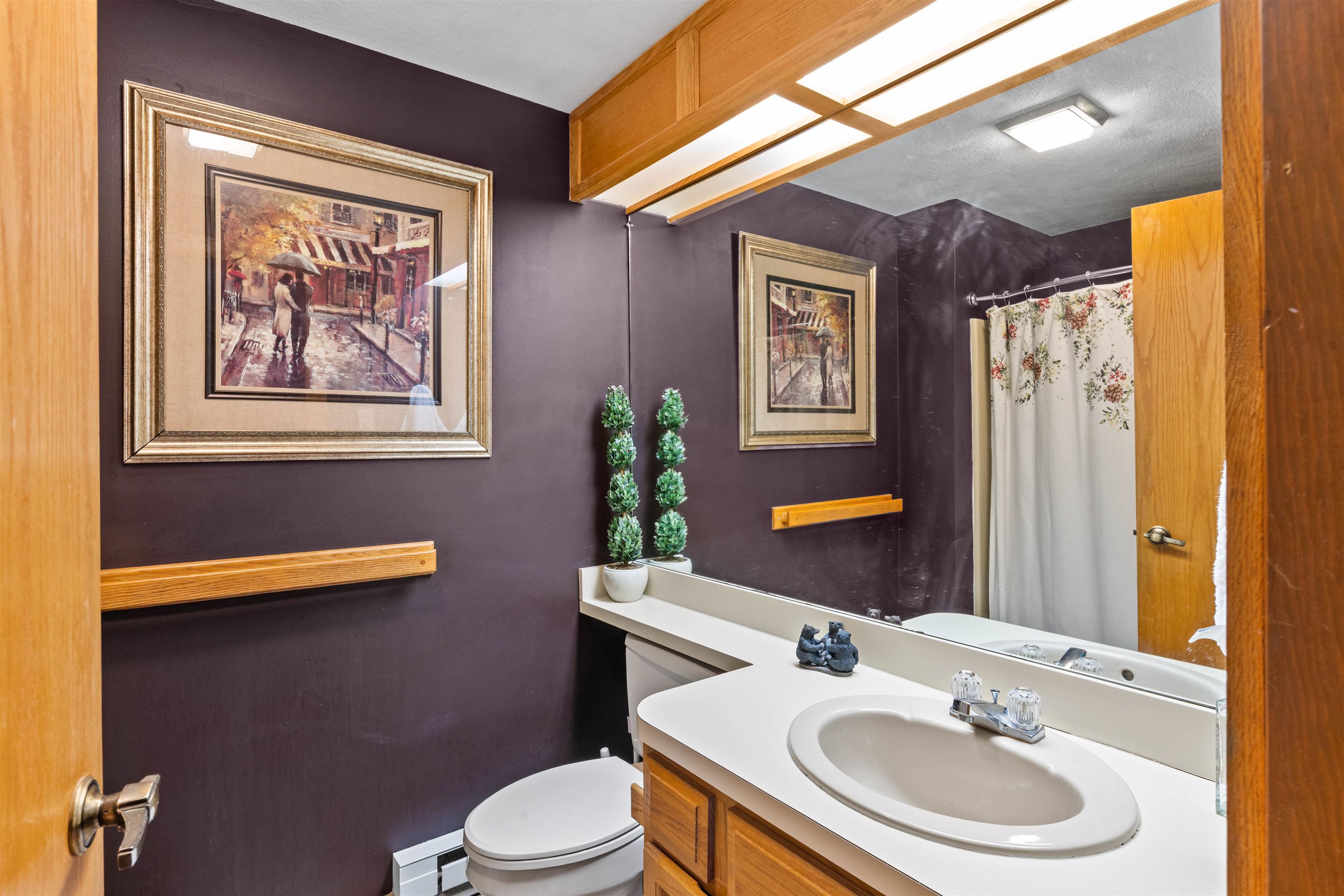 Bathroom with a wood vanity, large mirror, floral shower curtain, and dark purple walls.