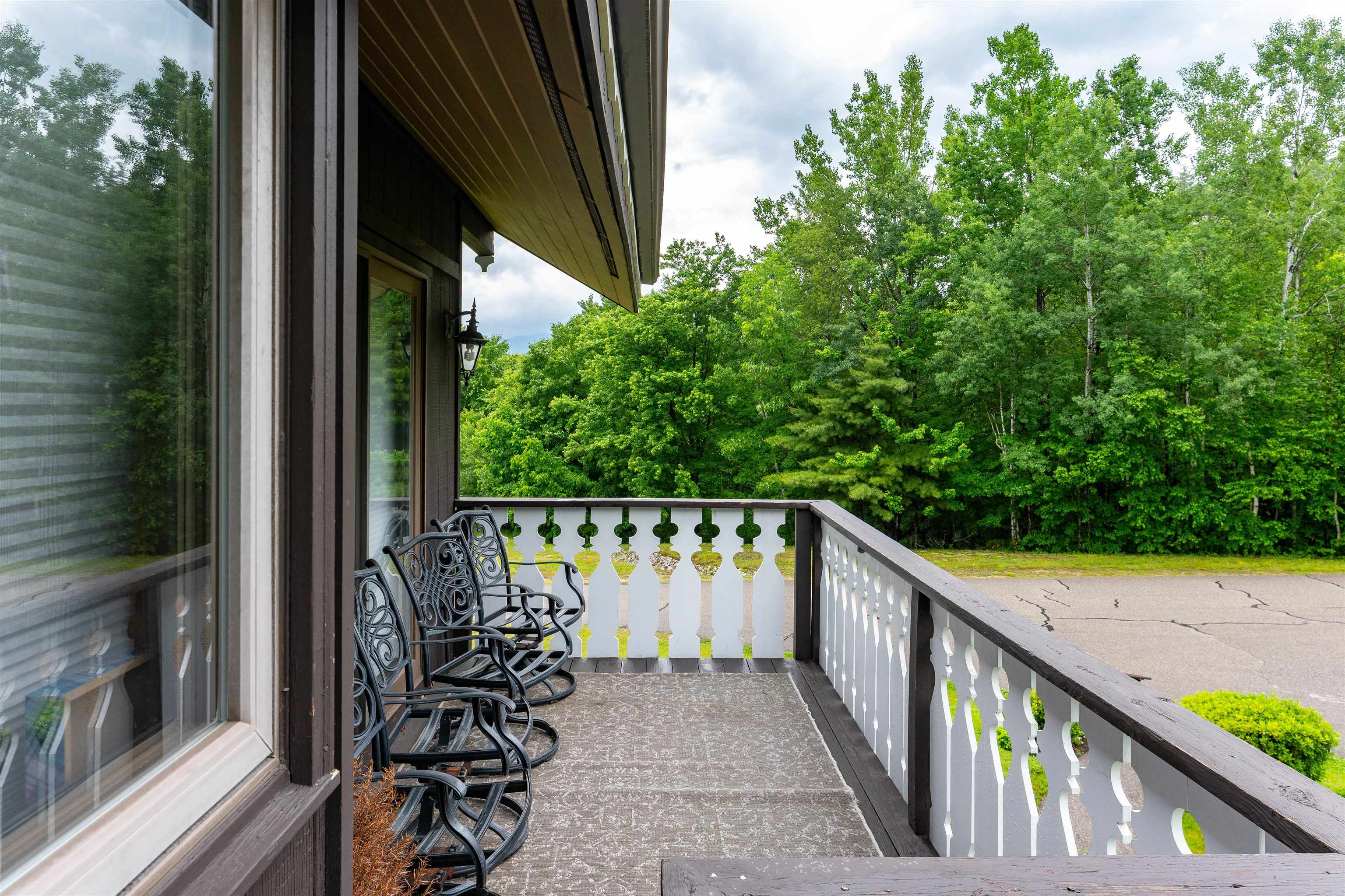 Balcony with ornate metal chairs and white railings overlooking leafy trees and a road.