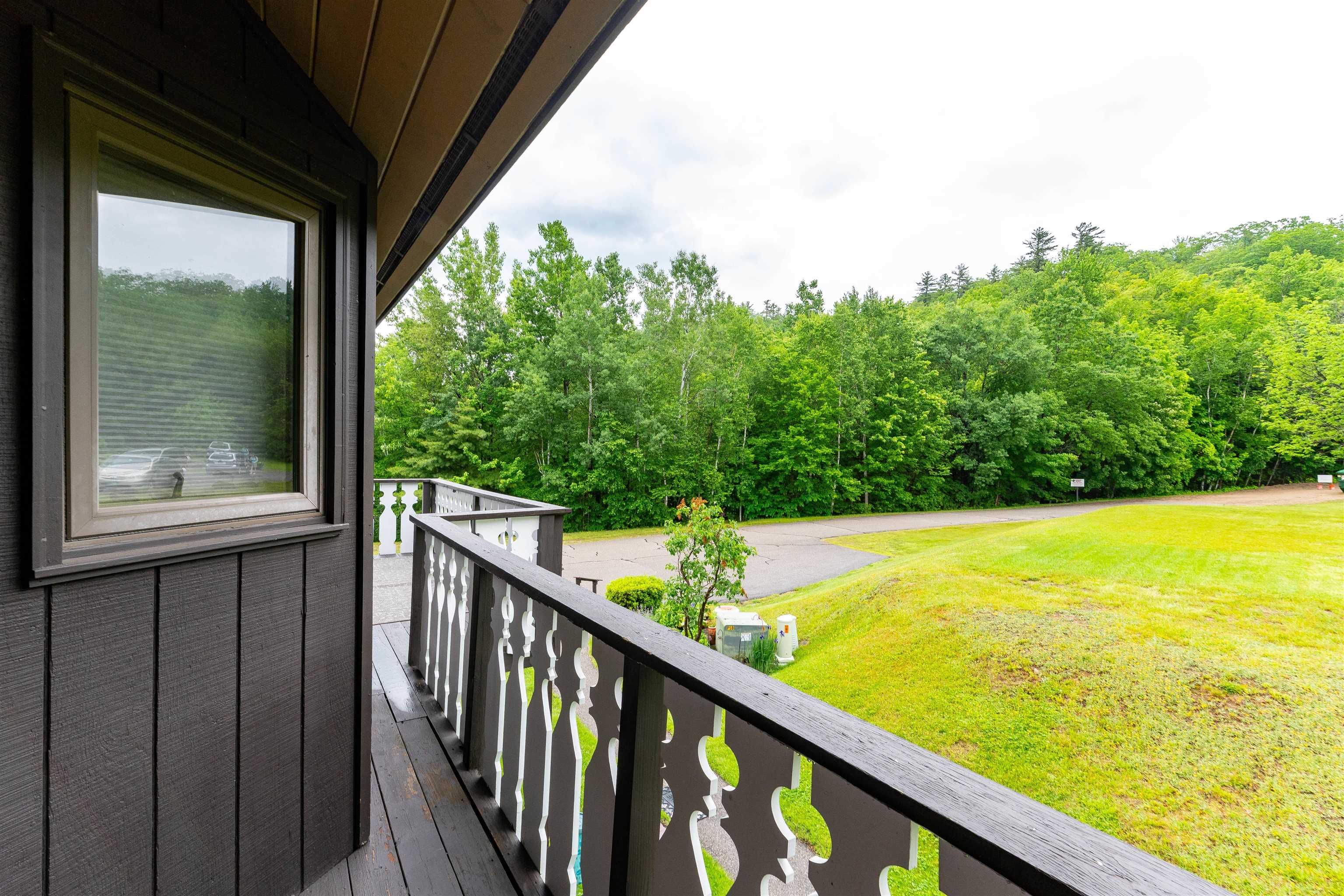Covered deck with white railing overlooking a grassy lawn and wooded hillside.