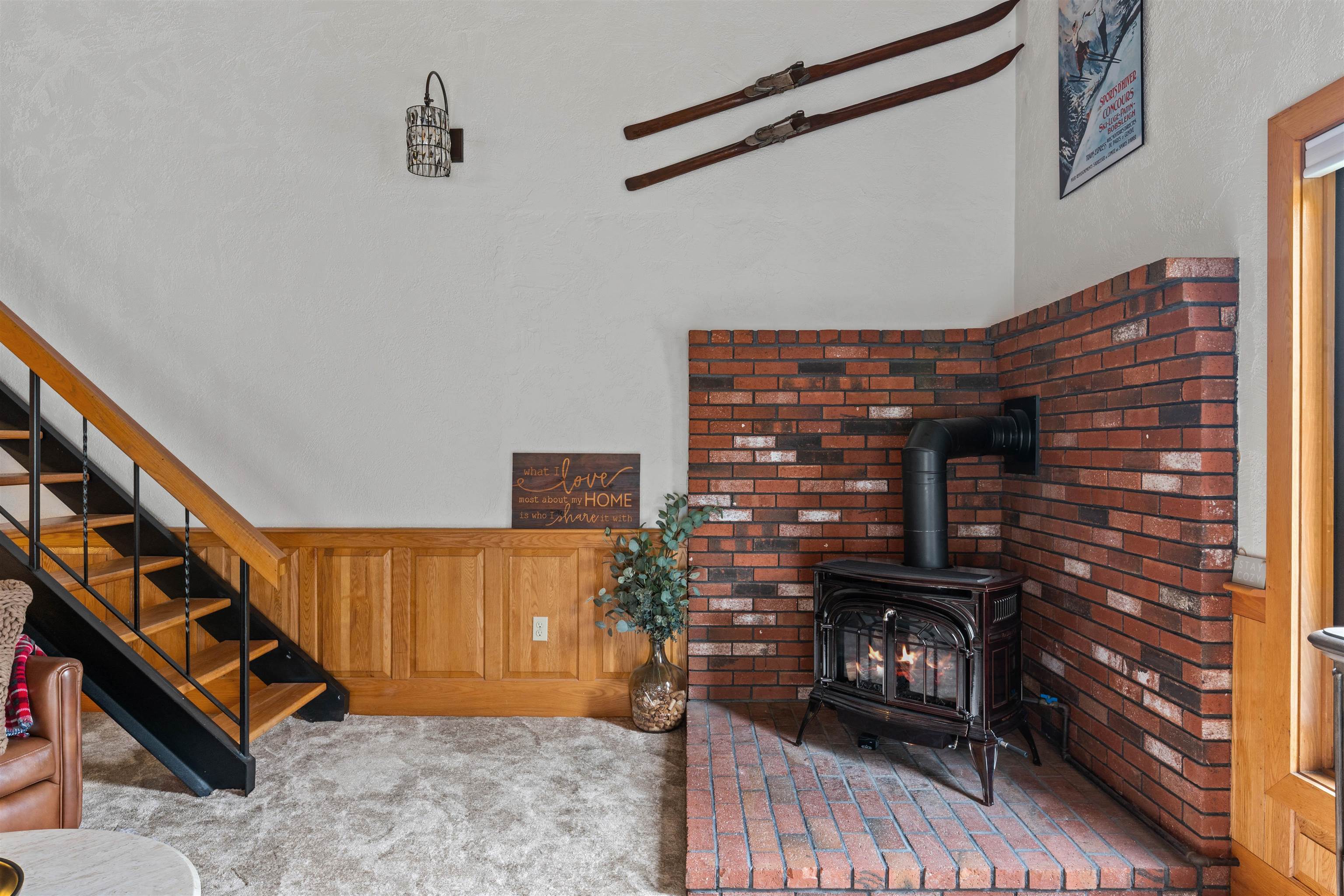 Living room with a black wood stove in a brick fireplace surround beside a wood-and-metal staircase.