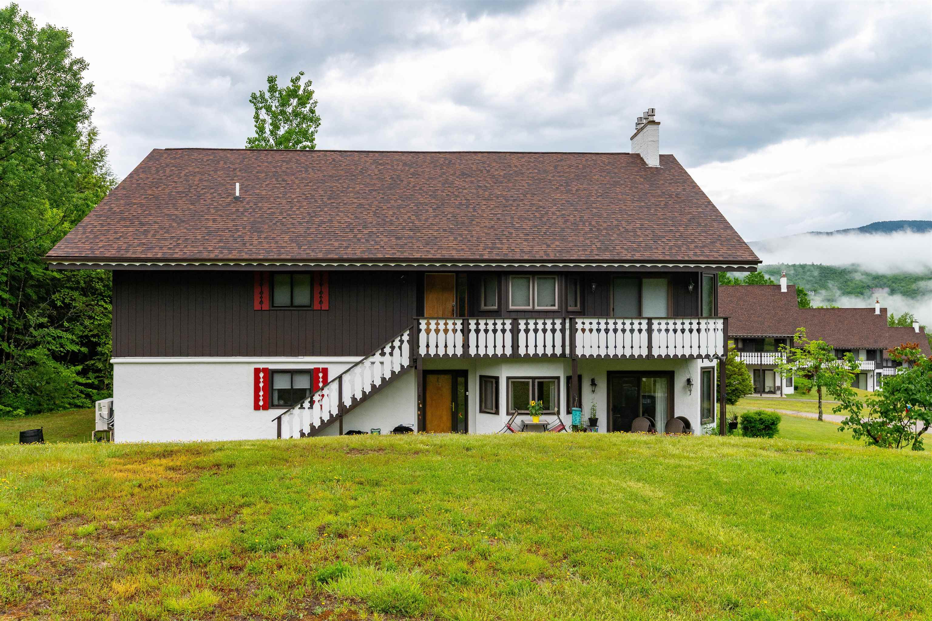 Two-story home with white balconies and an exterior staircase, set against a misty forested mountain ridge.