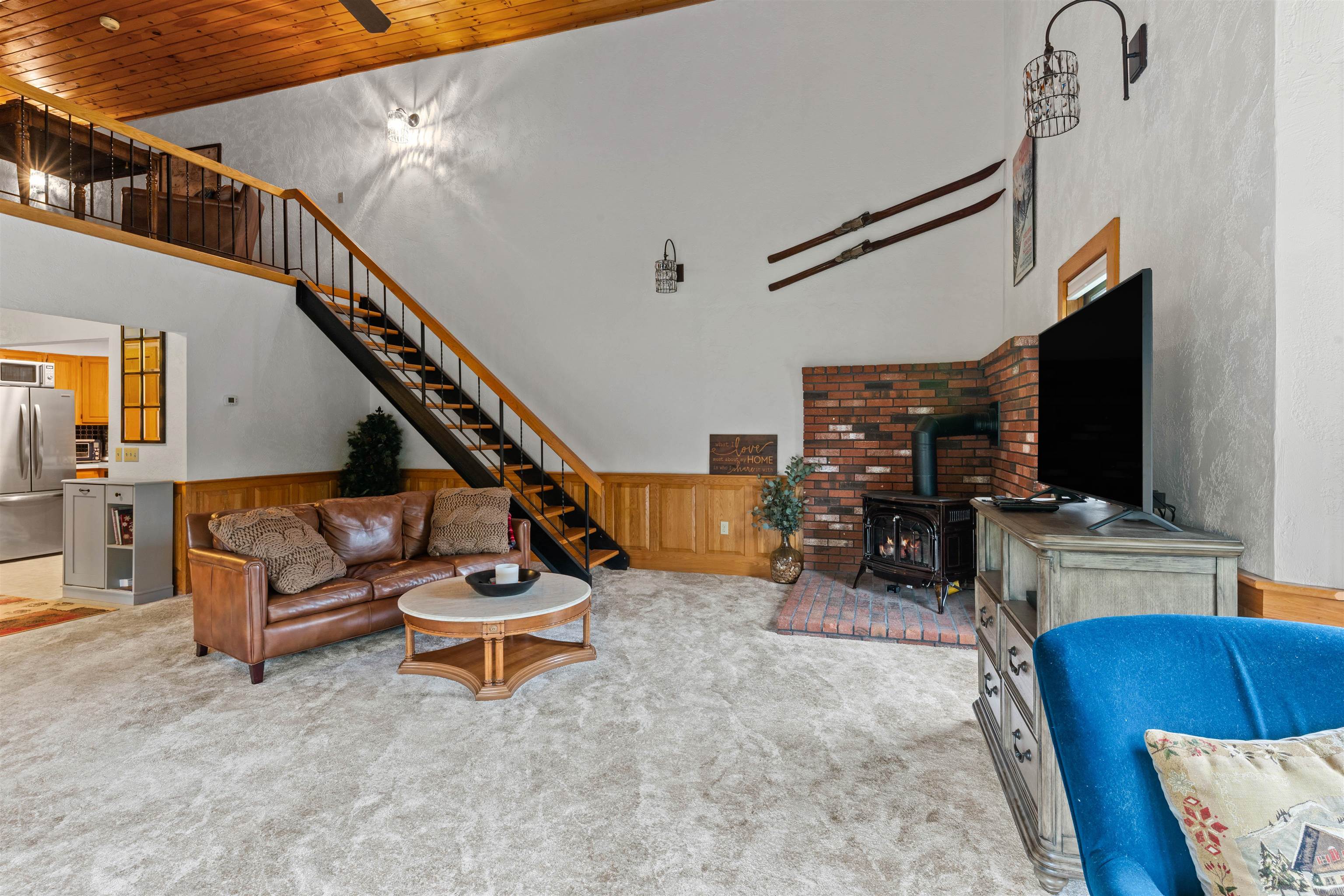 Furnished living room with a brick fireplace, wood stove, and open staircase.