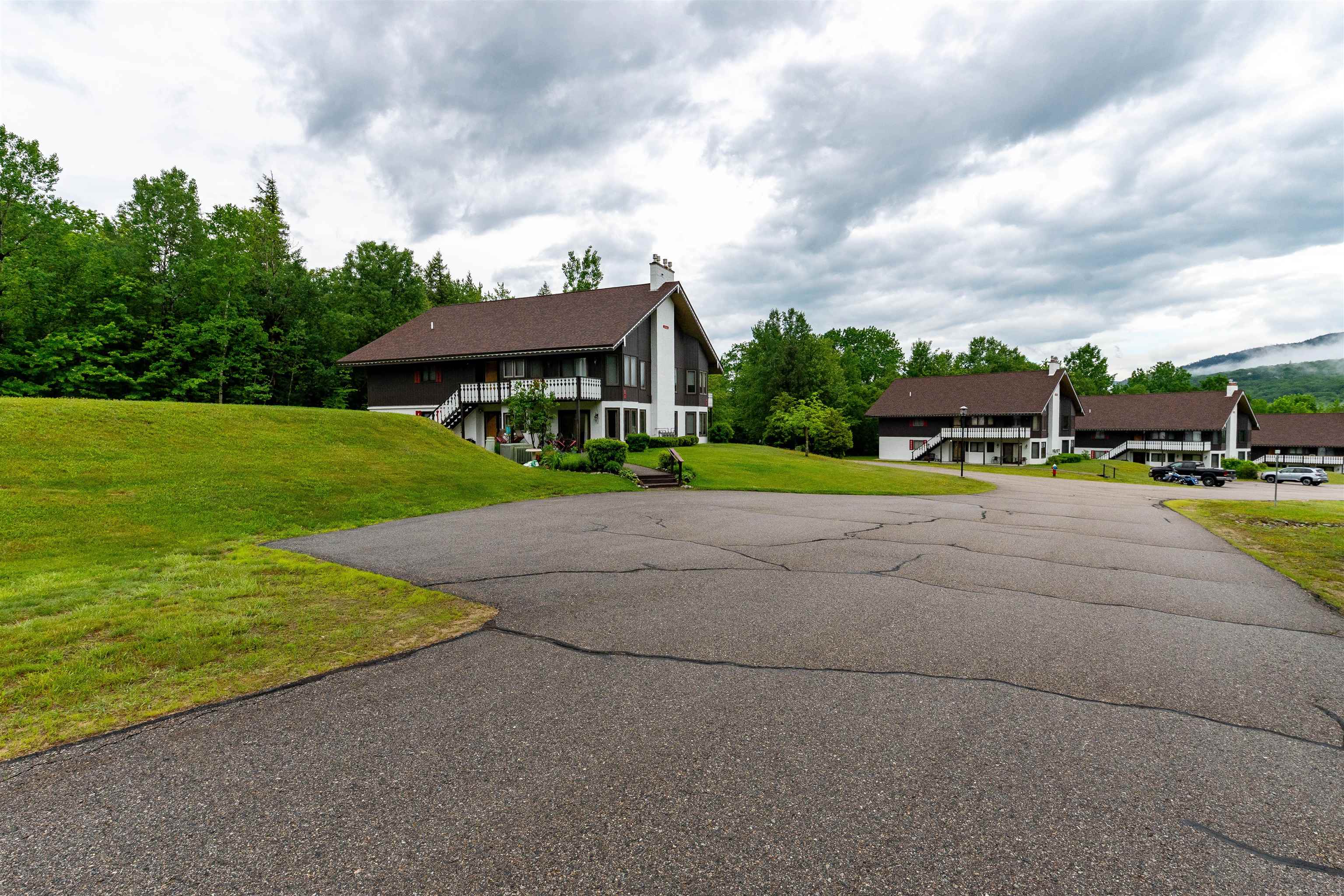 Multi-unit buildings with balconies beside a broad driveway, green lawns, and wooded hills.