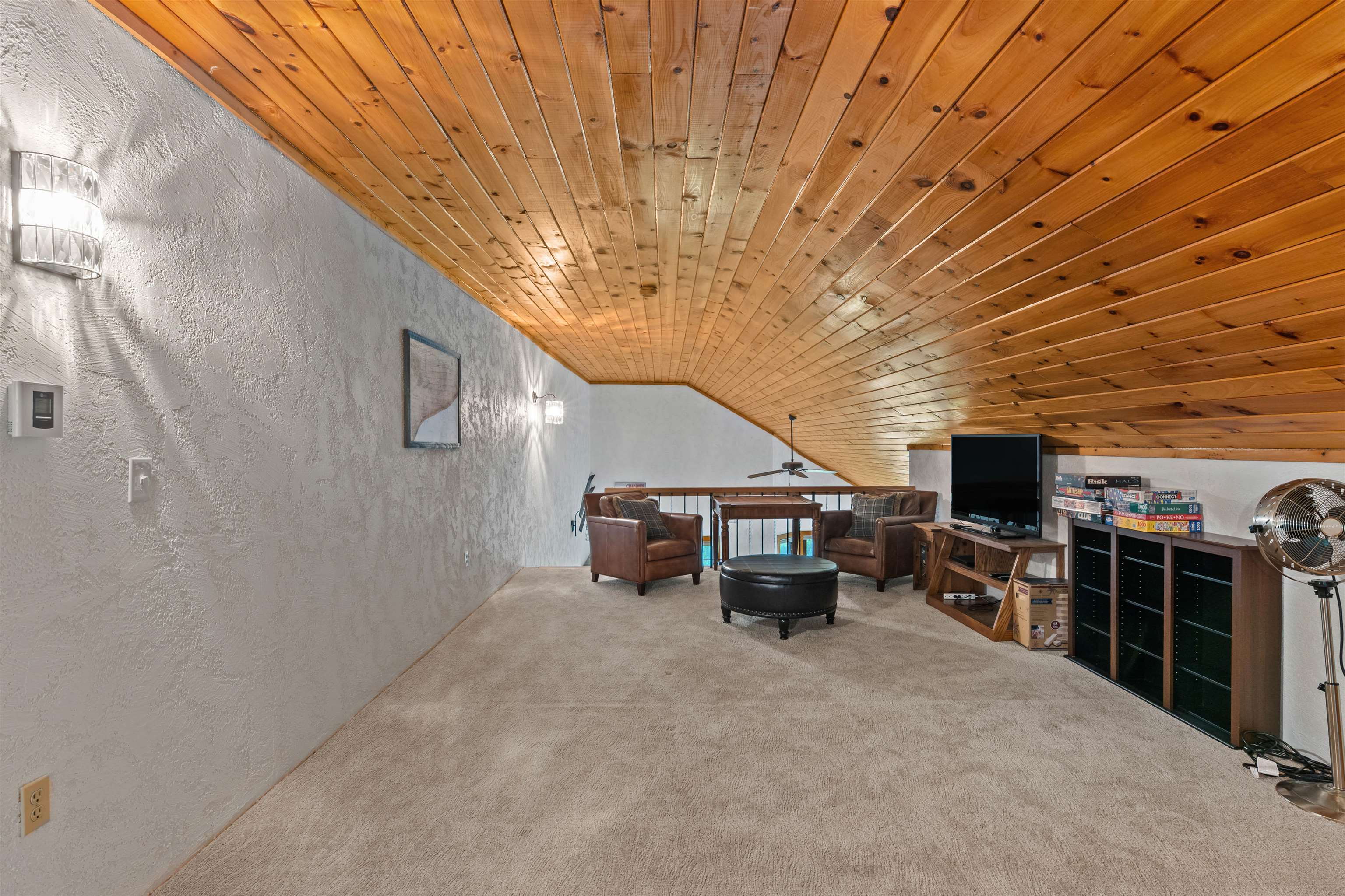 Furnished loft living area with a vaulted wood ceiling, leather armchairs, and television.