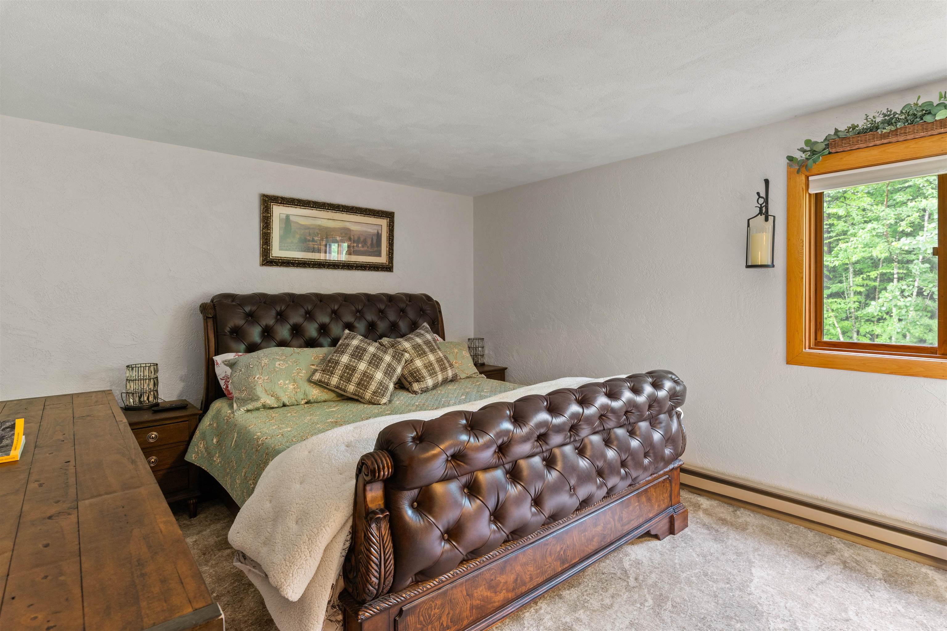 Bedroom with a tufted leather bed and a wood-trimmed window overlooking trees.