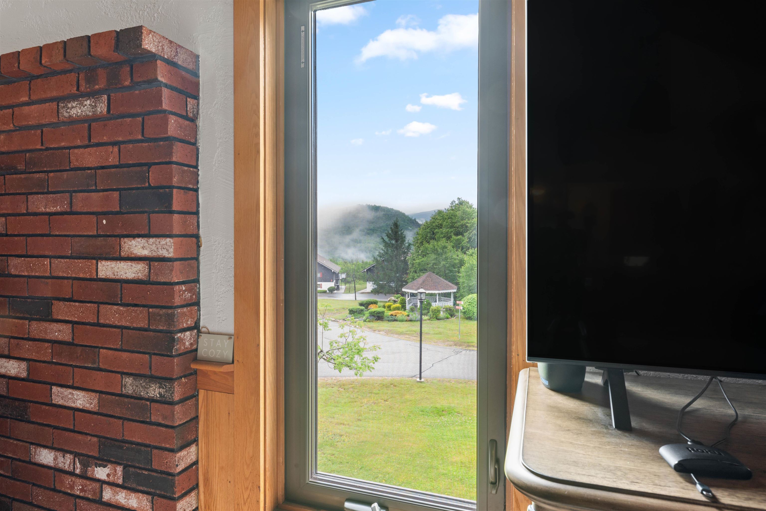 Room window overlooking misty green mountains, beside a brick fireplace and television.