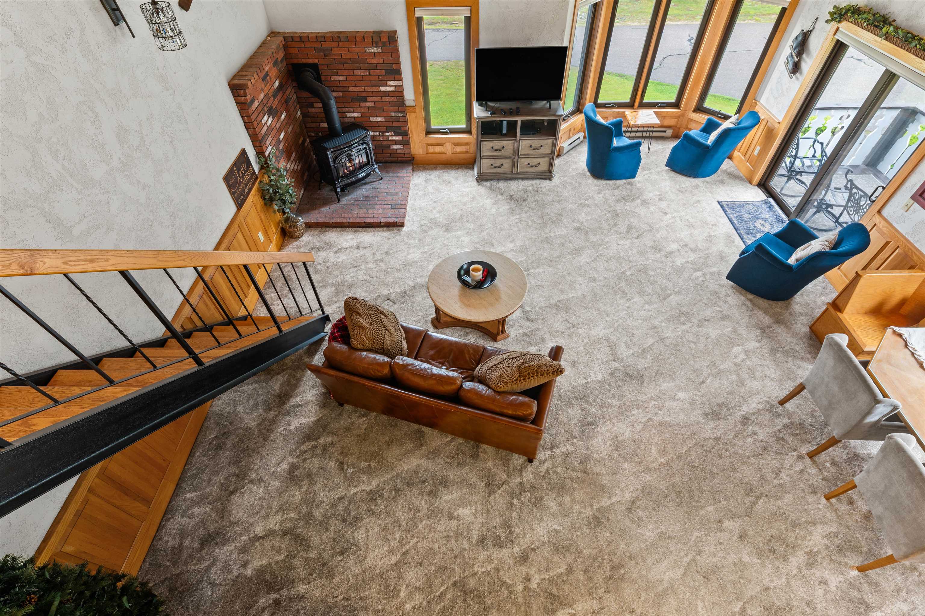 Furnished living room with brick hearth, wood stove, blue chairs, and tall windows.